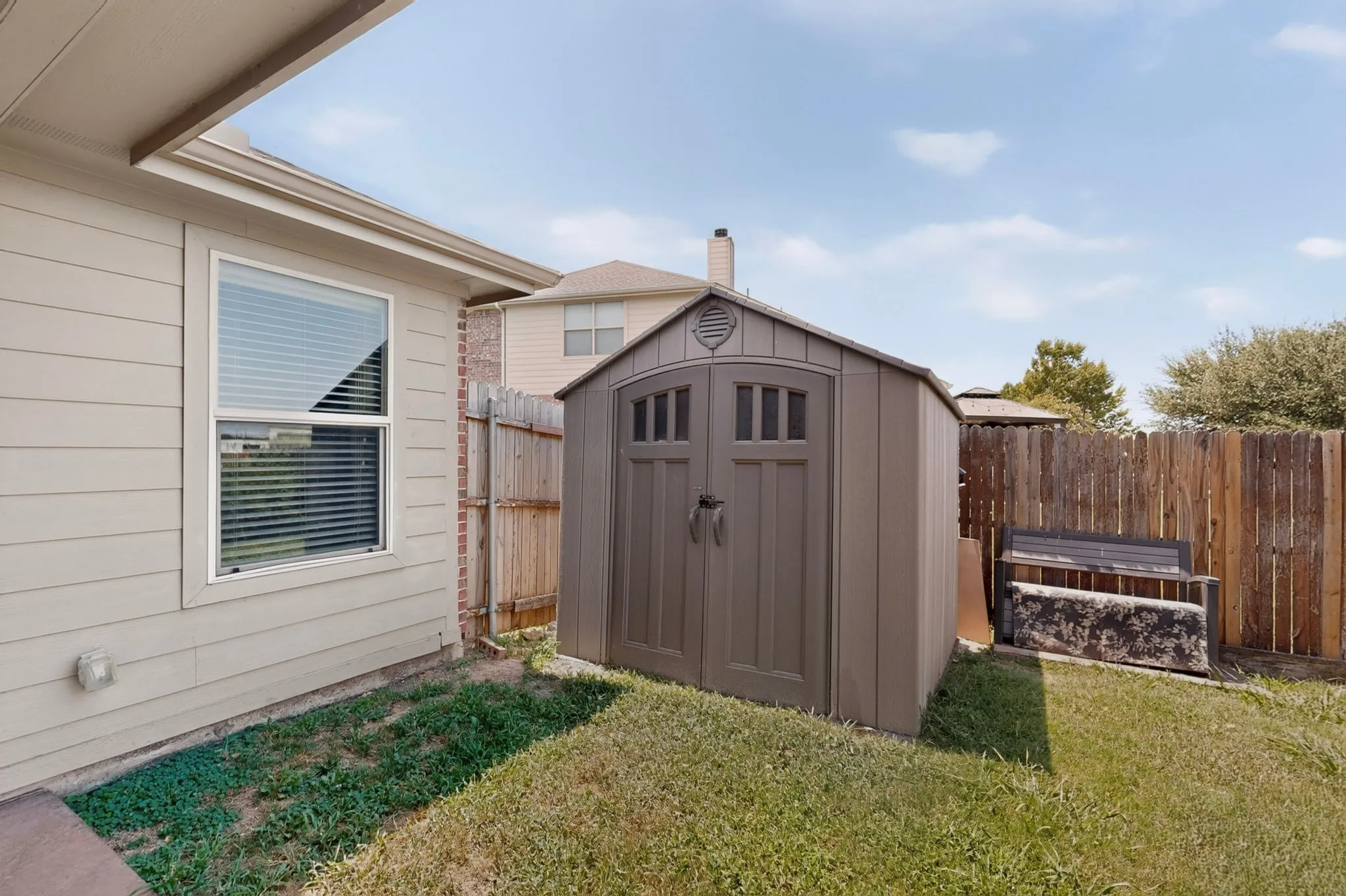 Siding exterior with a window, accompanied by a storage shed and a wooden fence