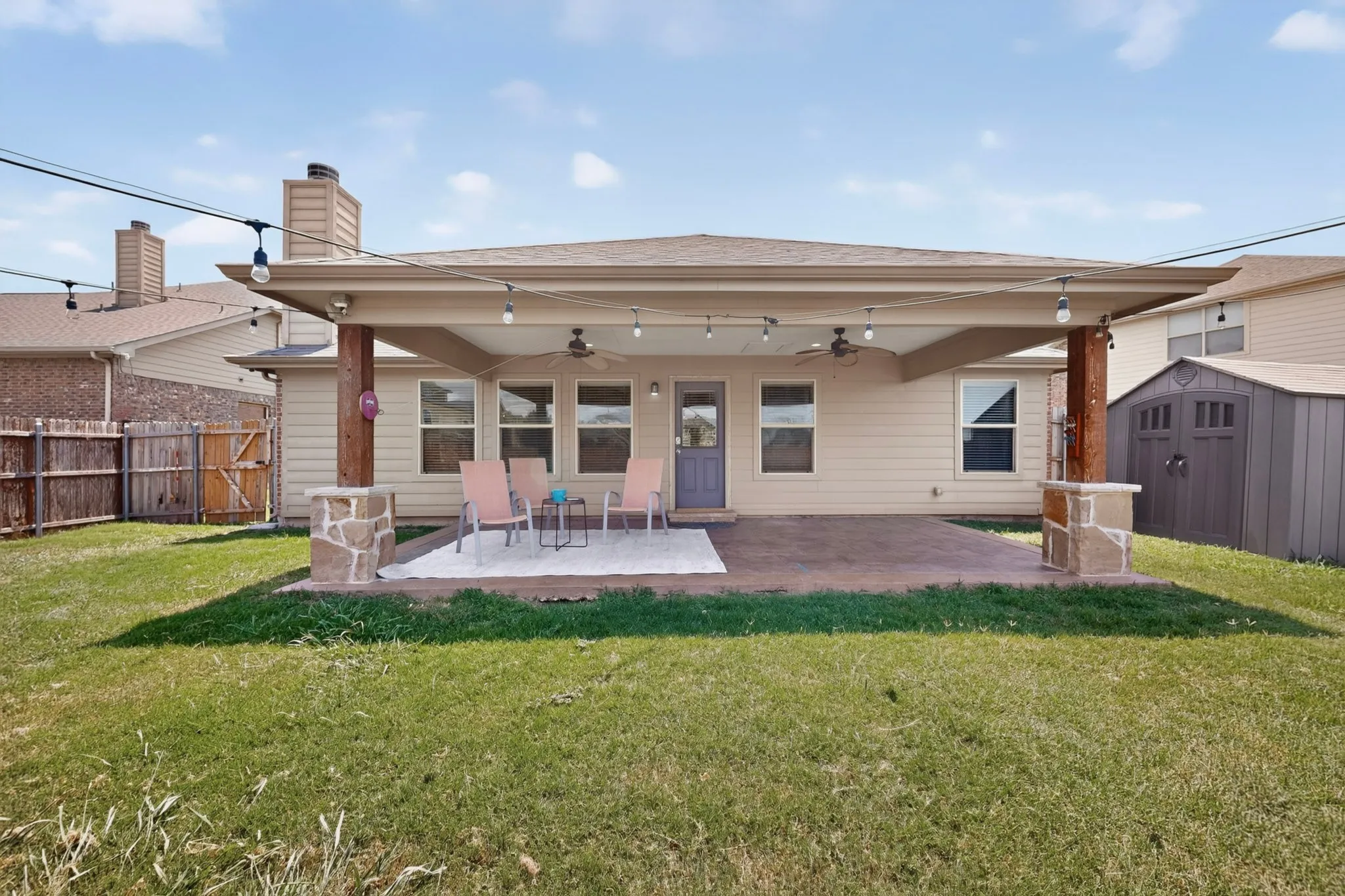Covered patio with stone-accented wood pillars, ceiling fans, and string lighting