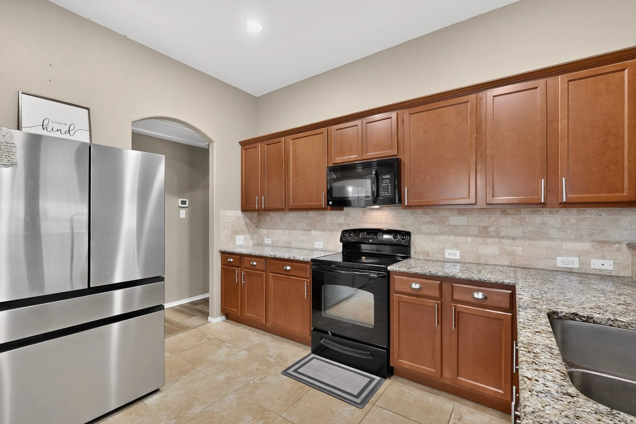 Kitchen featuring wood-finish cabinetry, granite countertops, tile flooring, and a tile backsplash