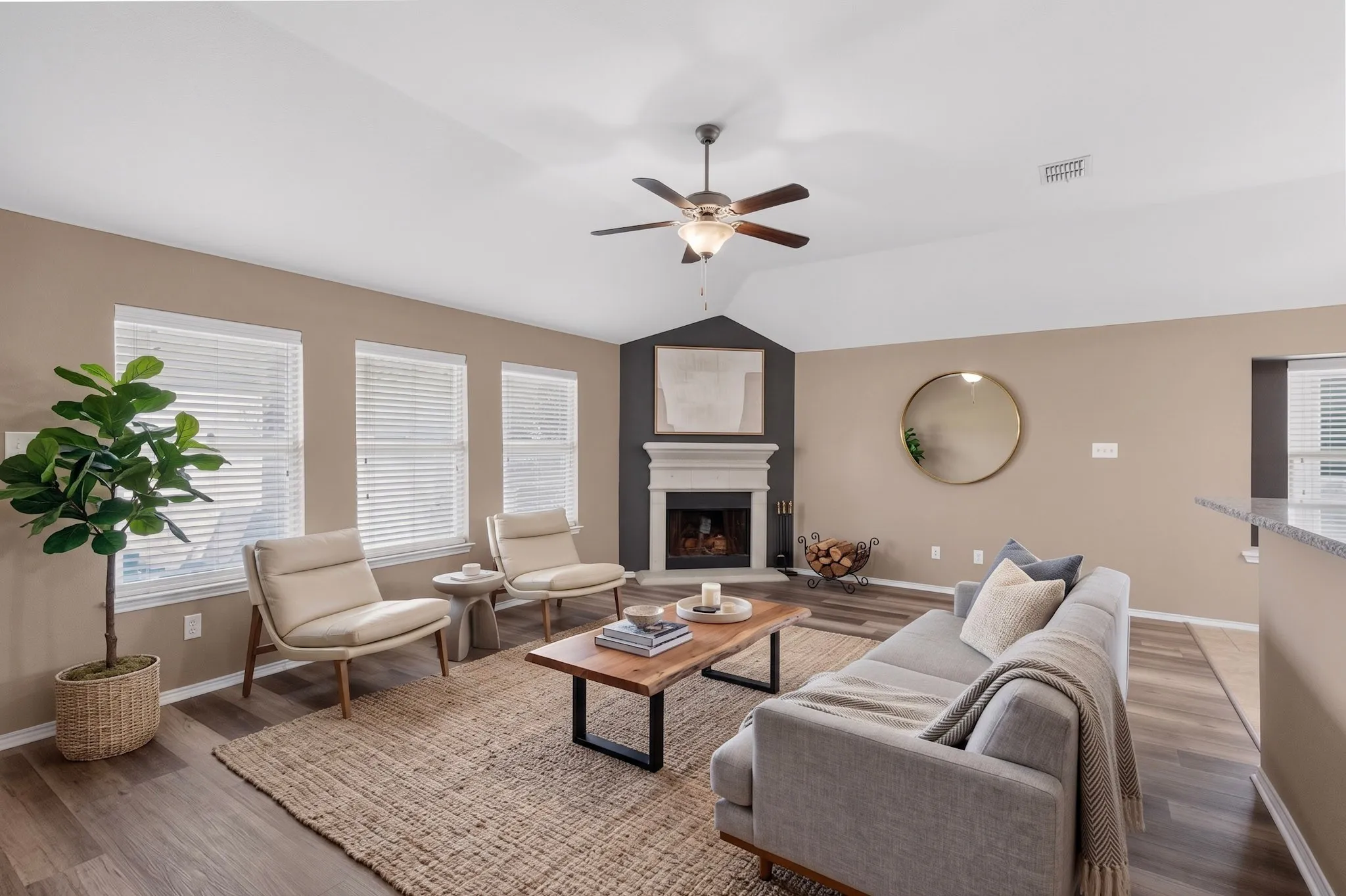 Vaulted ceiling with a ceiling fan, fireplace with a mantel, wood-finish flooring, multiple windows, and a built-in breakfast bar