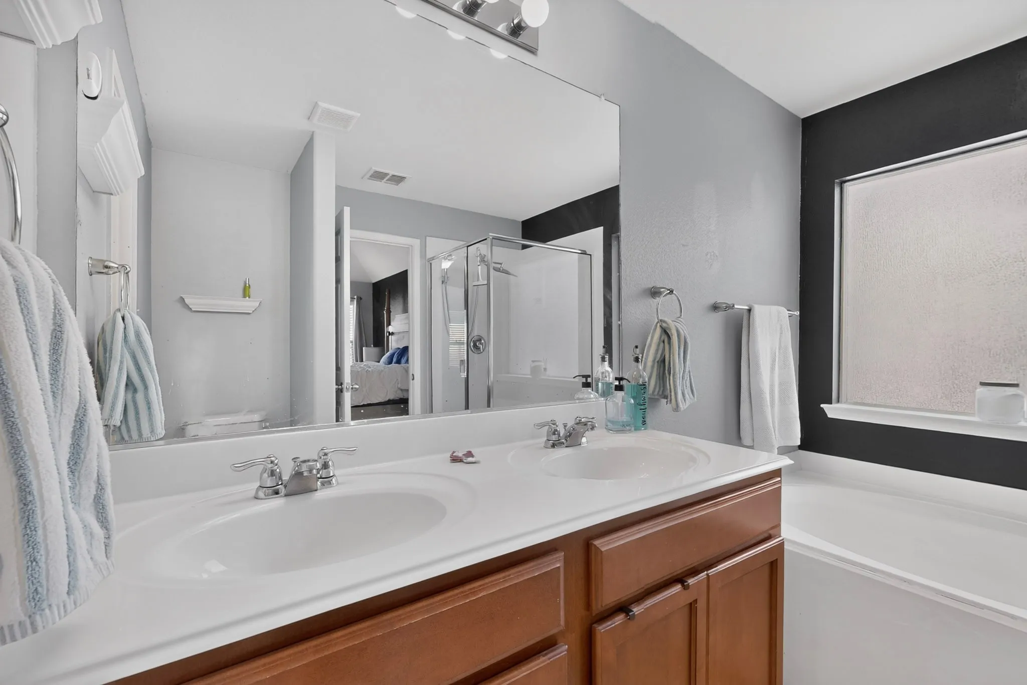 Dual sink vanity with wood-finish cabinetry, chrome fixtures, and a large integrated mirror