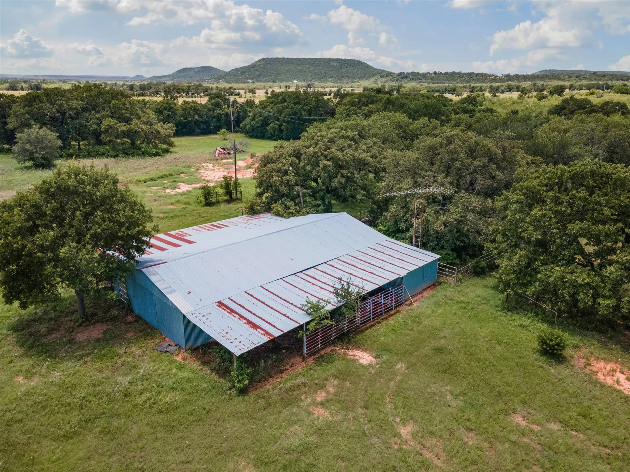 Metal barn structure featuring an attached covered area with visible fencing