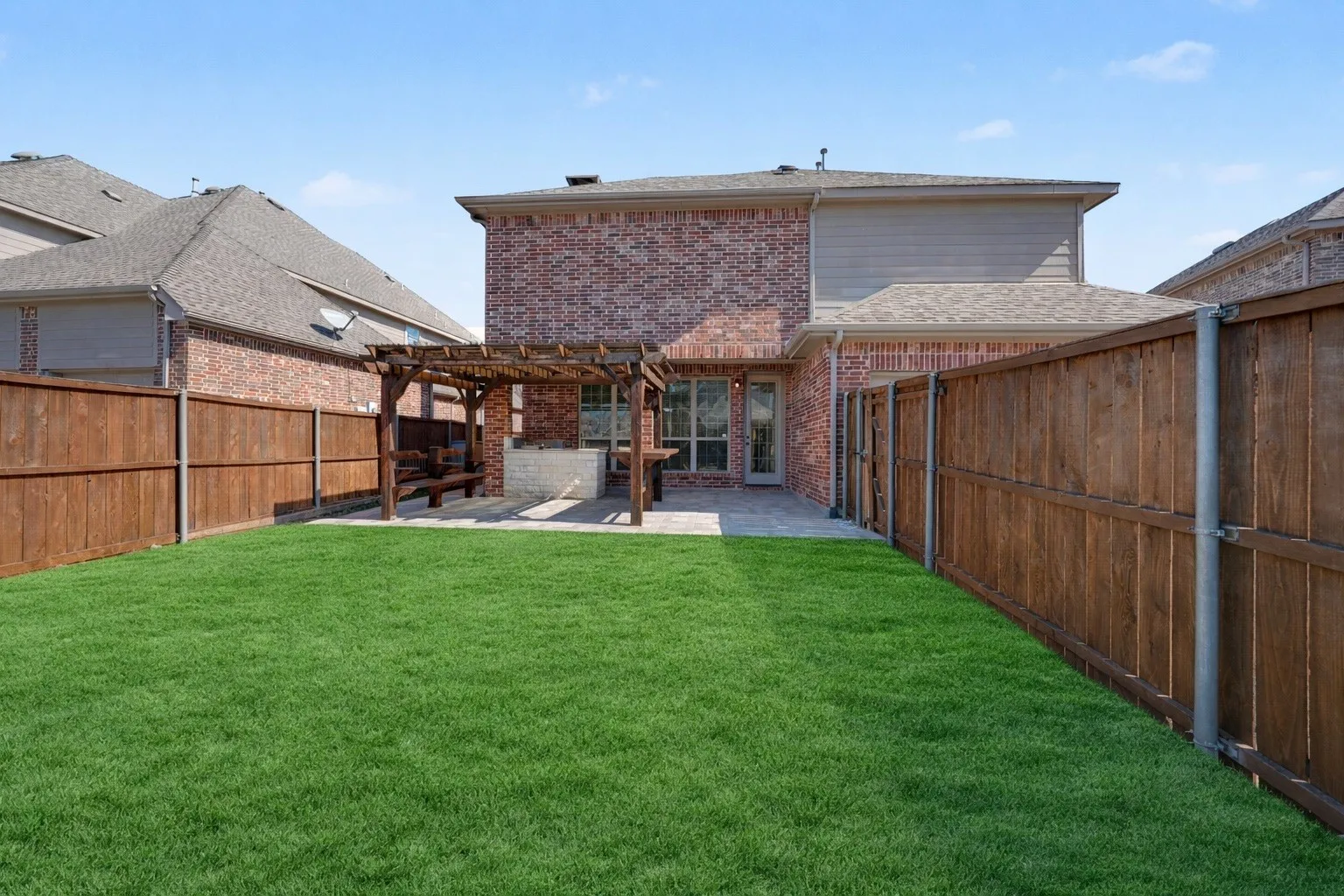 Expansive backyard featuring a stone patio, a wooden pergola, and a privacy fence