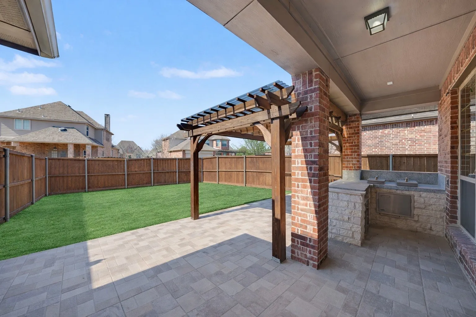 Covered patio with paver flooring, integrated outdoor kitchen, and a wooden pergola