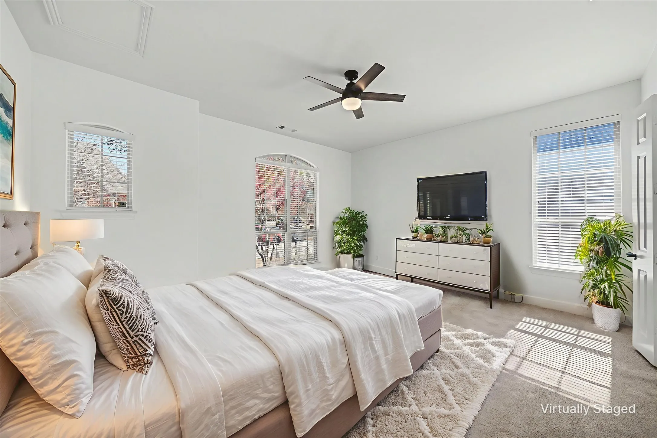 Bright bedroom featuring arched window, additional window with blinds, ceiling fan with light, and carpeted flooring