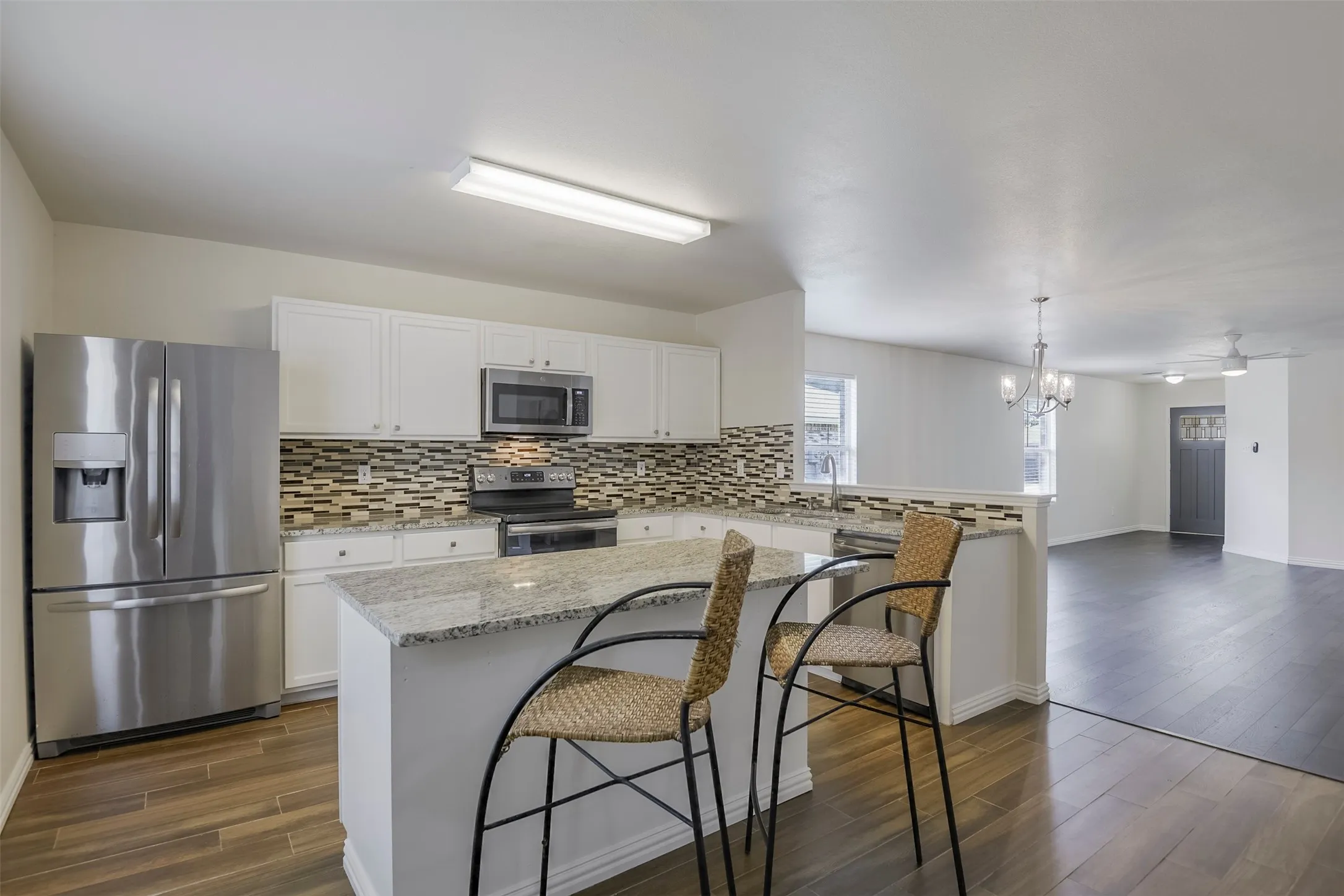 Kitchen featuring stainless steel appliances, white cabinetry, a mosaic tile backsplash, and a granite island with breakfast bar seating