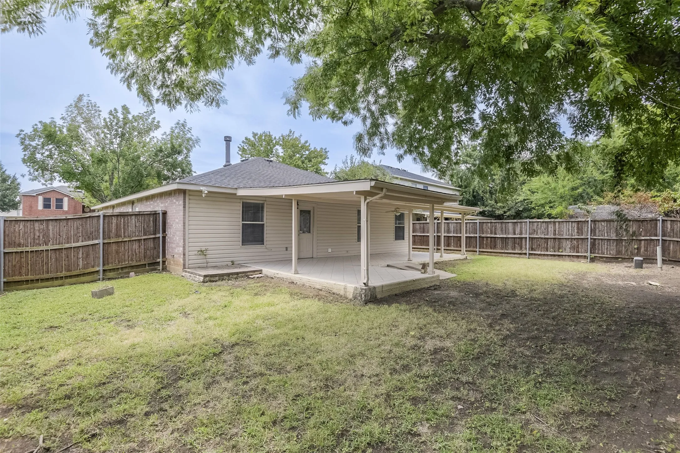 Expansive backyard featuring a covered patio, wood privacy fencing, and mature perimeter trees