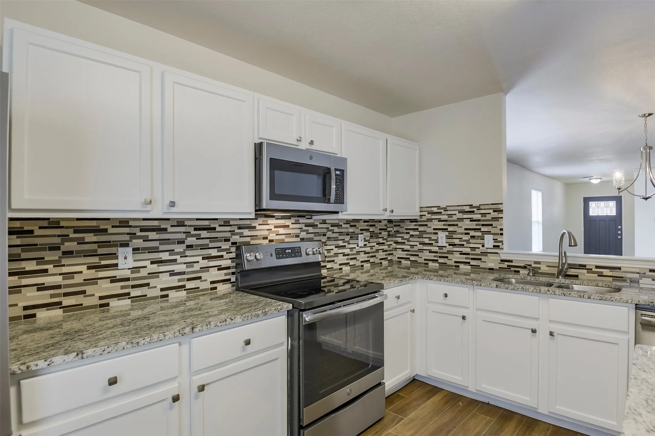Kitchen featuring white cabinetry, stone countertops, a tile backsplash, stainless steel appliances, and wood-finish flooring
