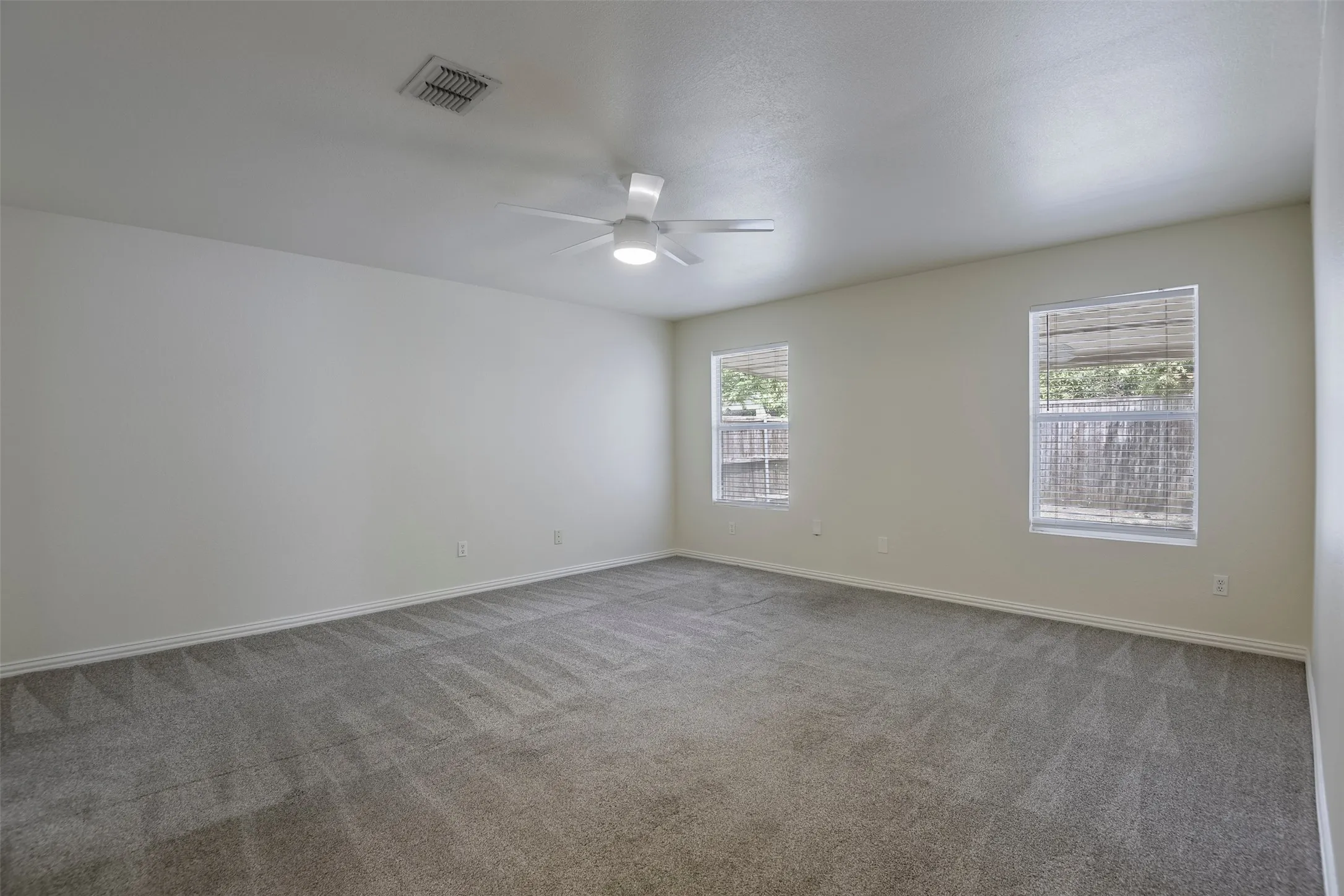 Spacious room featuring neutral paint, gray patterned carpeting, and two windows with blinds