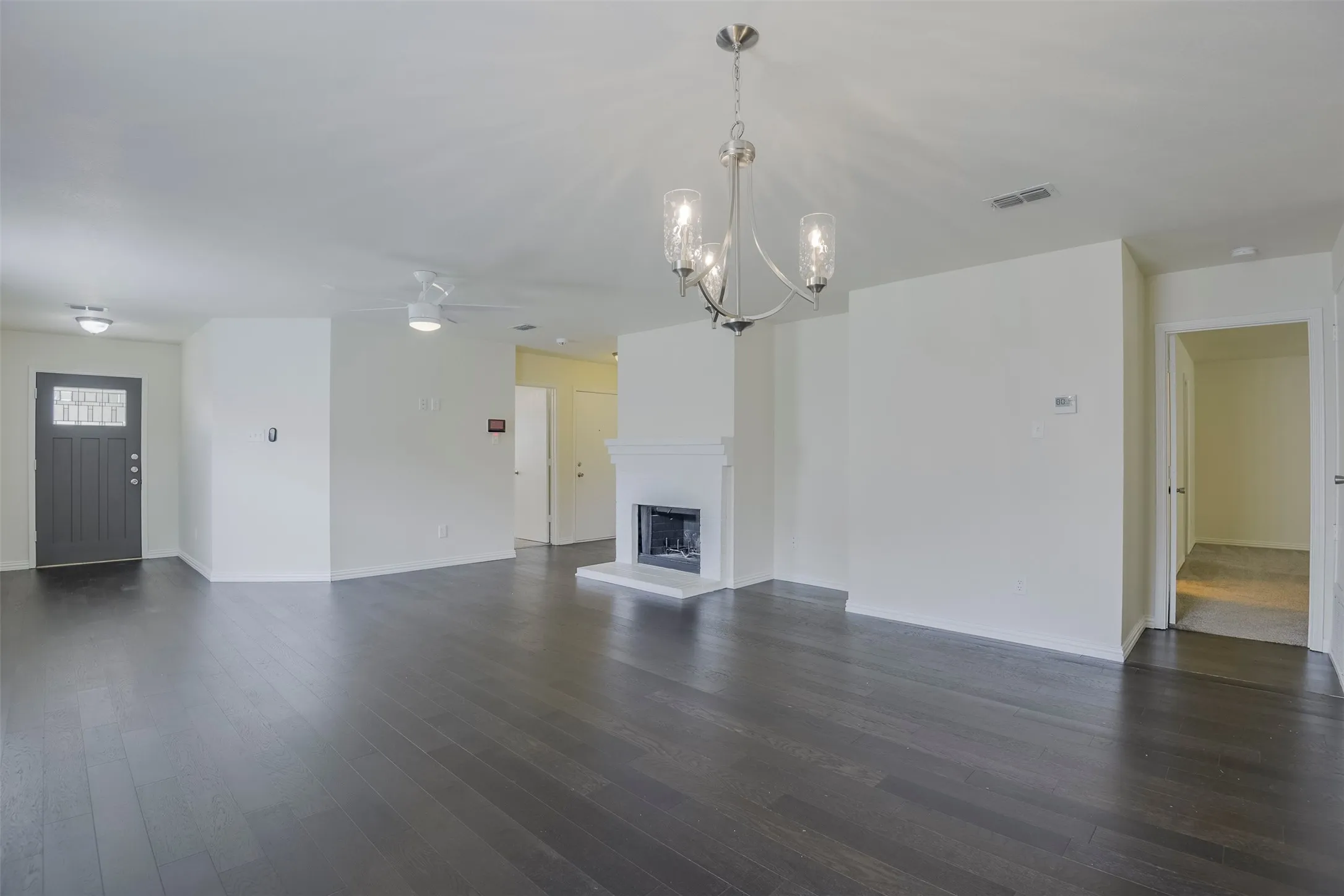 Spacious room featuring dark wood-finish flooring, a white mantel fireplace, and a contemporary chandelier