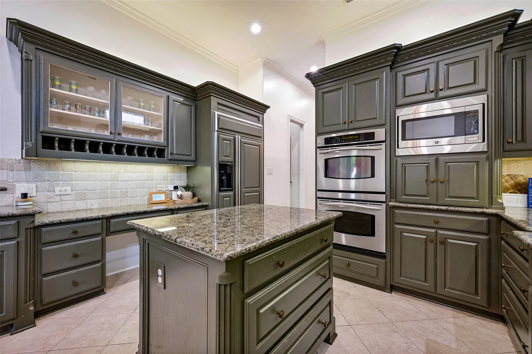 Kitchen featuring a central island with granite countertop, extensive cabinetry, integrated stainless steel appliances, and a tiled backsplash