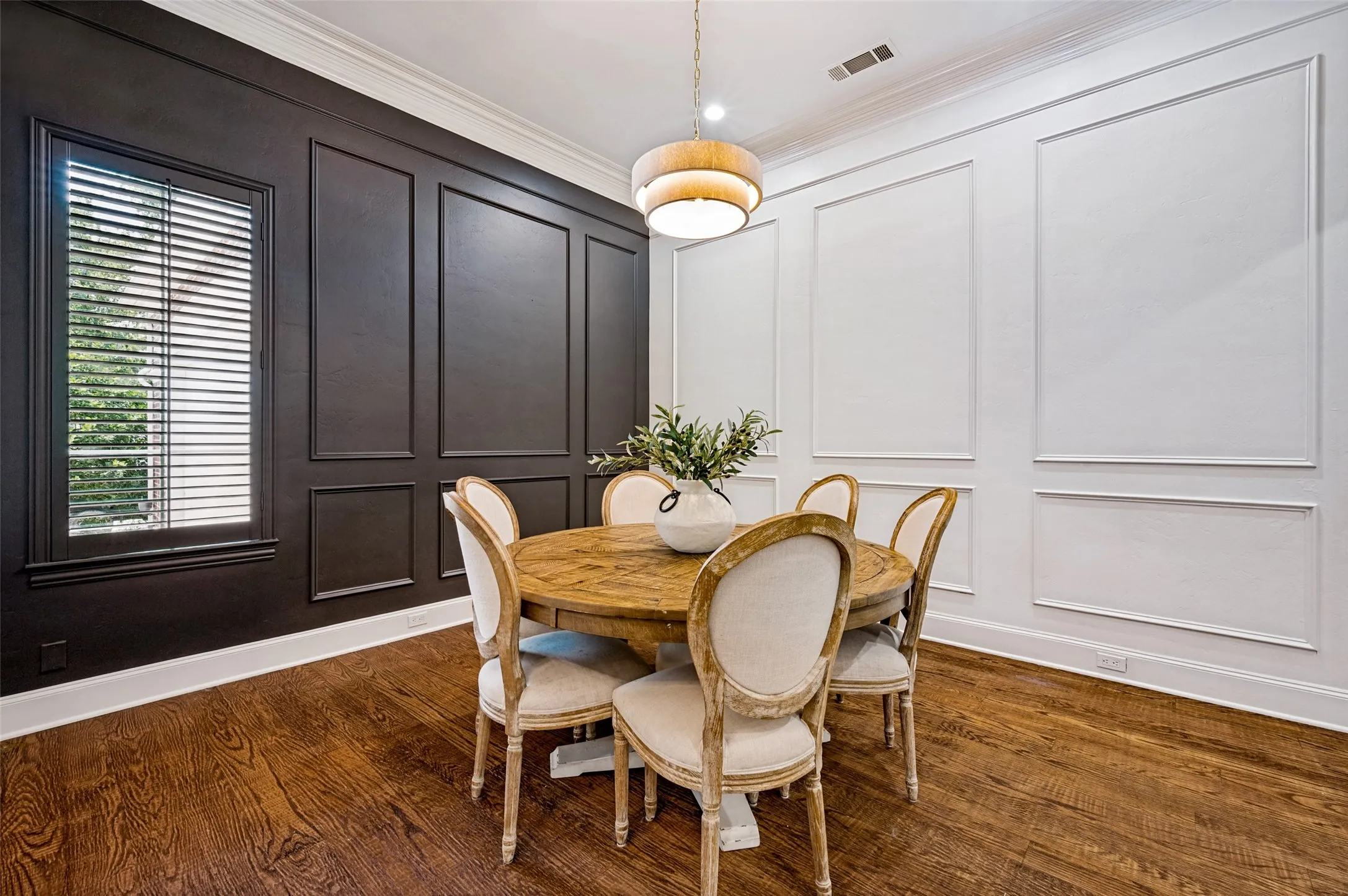 Dark paneled accent wall, white decorative wall molding, wood-finish flooring, white crown molding, and a drum pendant light fixture