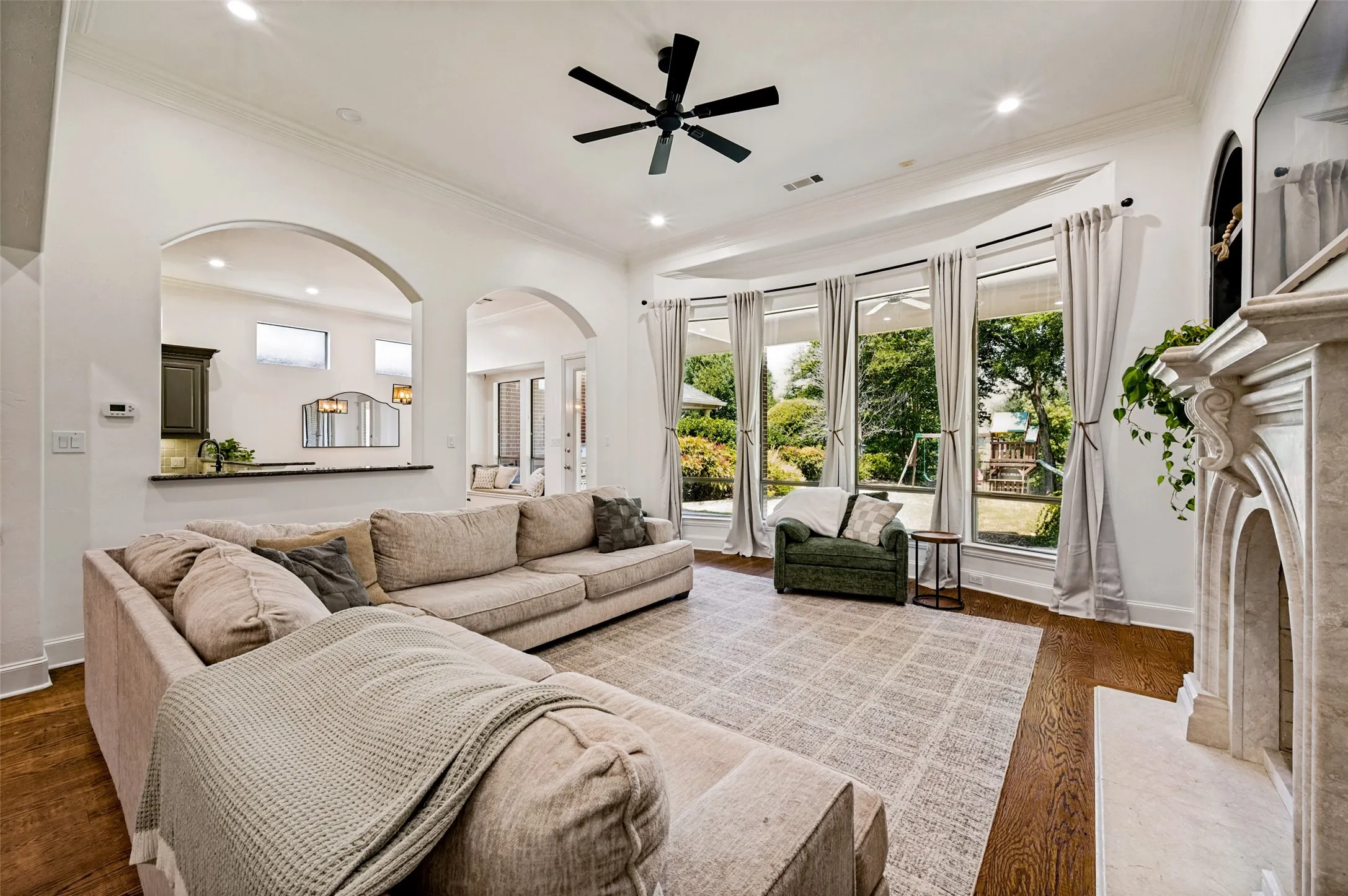 Spacious living area featuring a decorative fireplace, large bay windows, wood-finish flooring, and arched interior openings