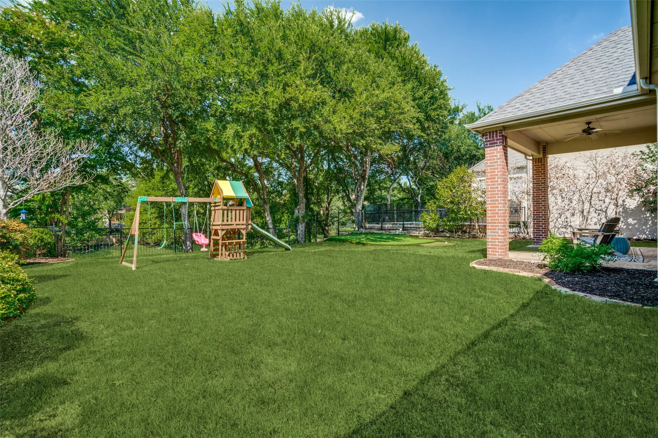 Expansive lawn with mature trees and a covered patio featuring brick columns and a ceiling fan