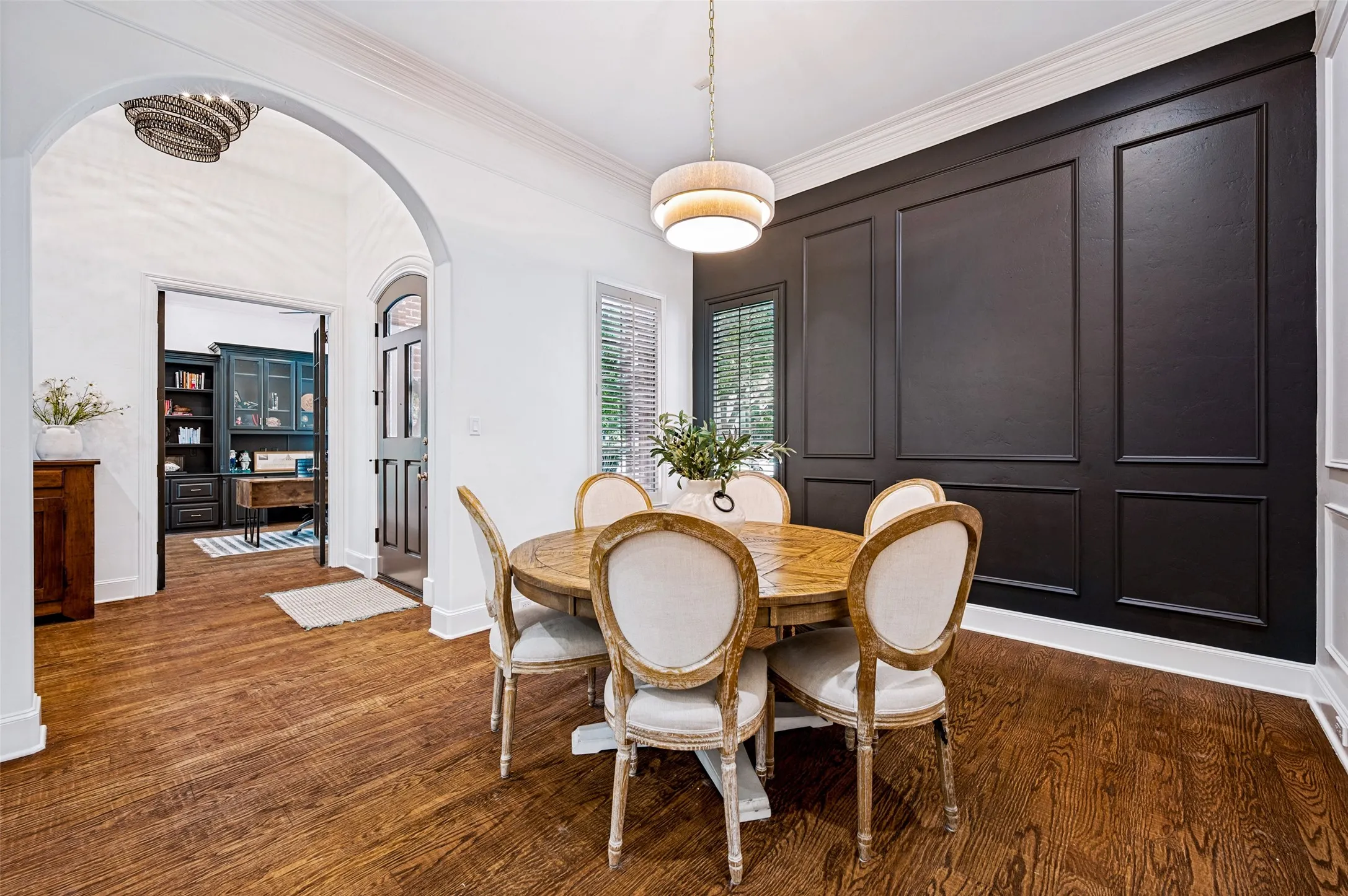Rich wood-finish flooring, accent wall with decorative paneling, arched doorway, and built-in cabinetry