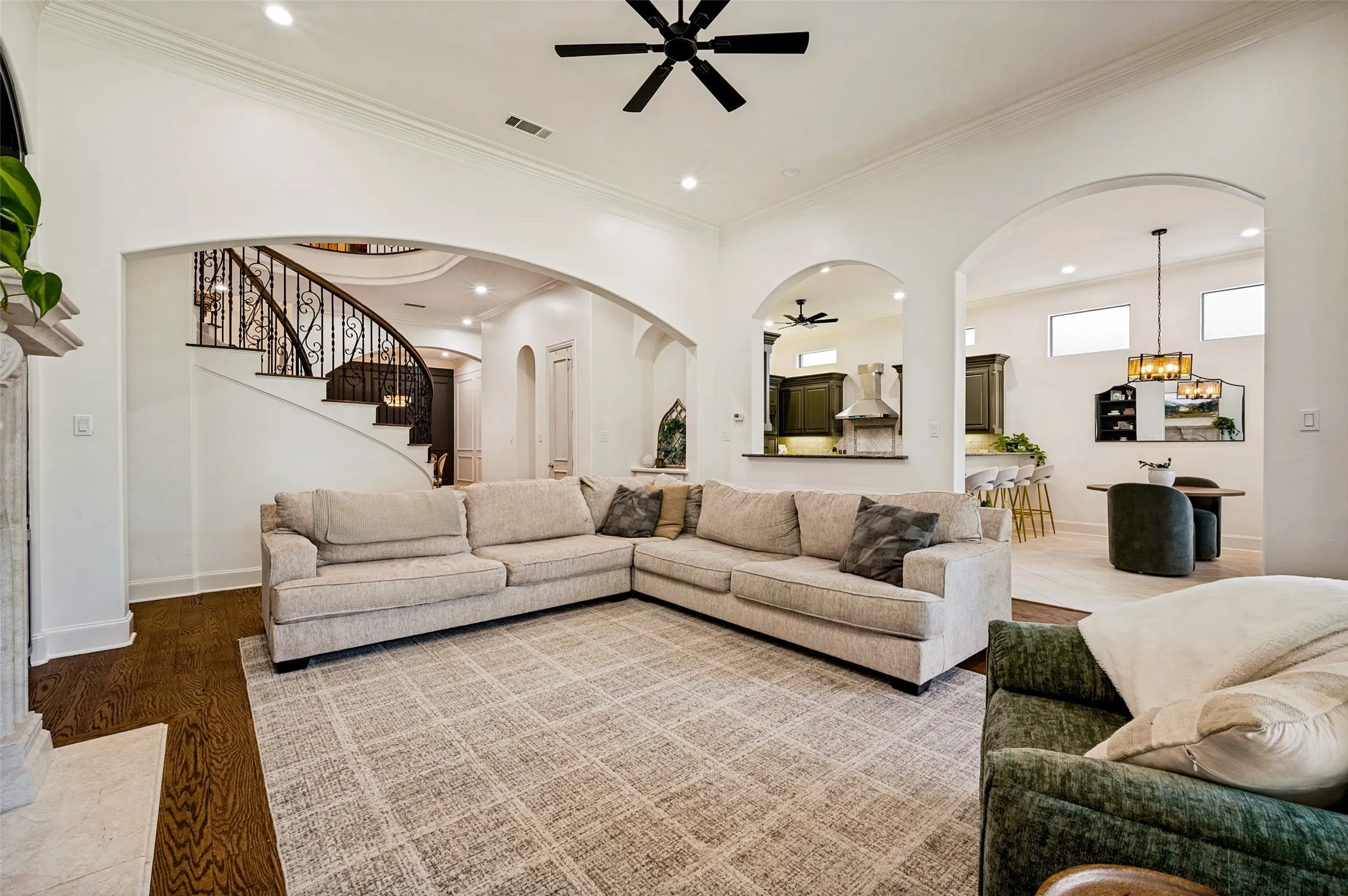 Hardwood flooring, arched doorways, recessed lighting, crown molding, and an ornate wrought-iron staircase