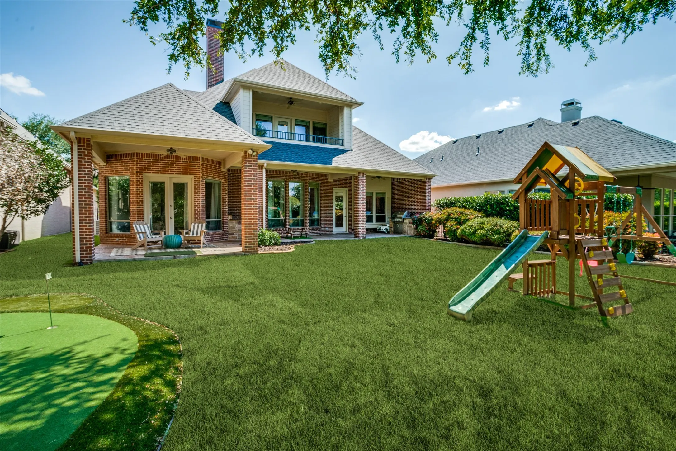 Expansive backyard featuring a putting green, covered patio, and brick exterior