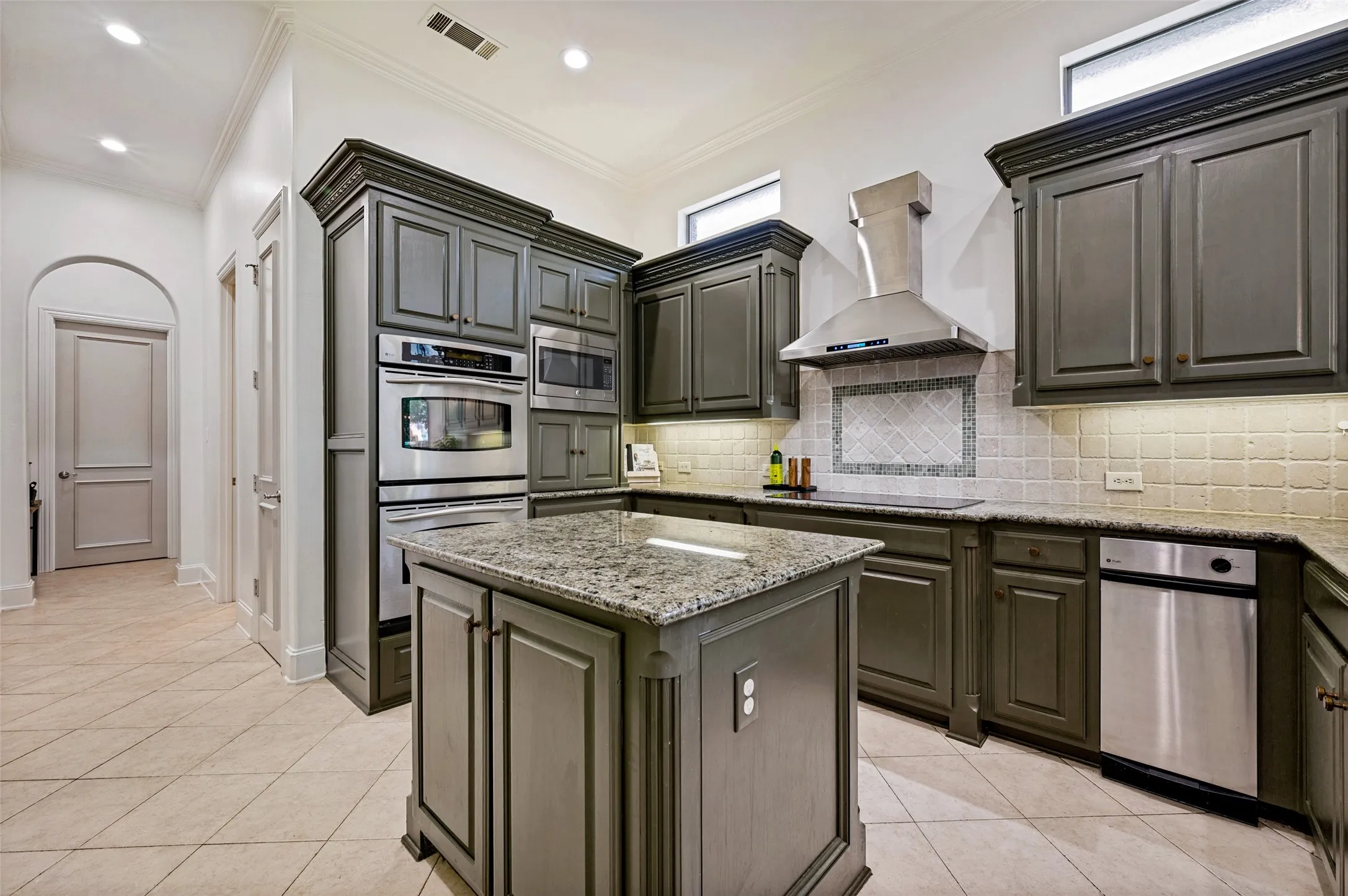 Kitchen featuring custom cabinetry, stainless steel appliances, granite countertops, a tiled backsplash, and an integrated island with a granite surface