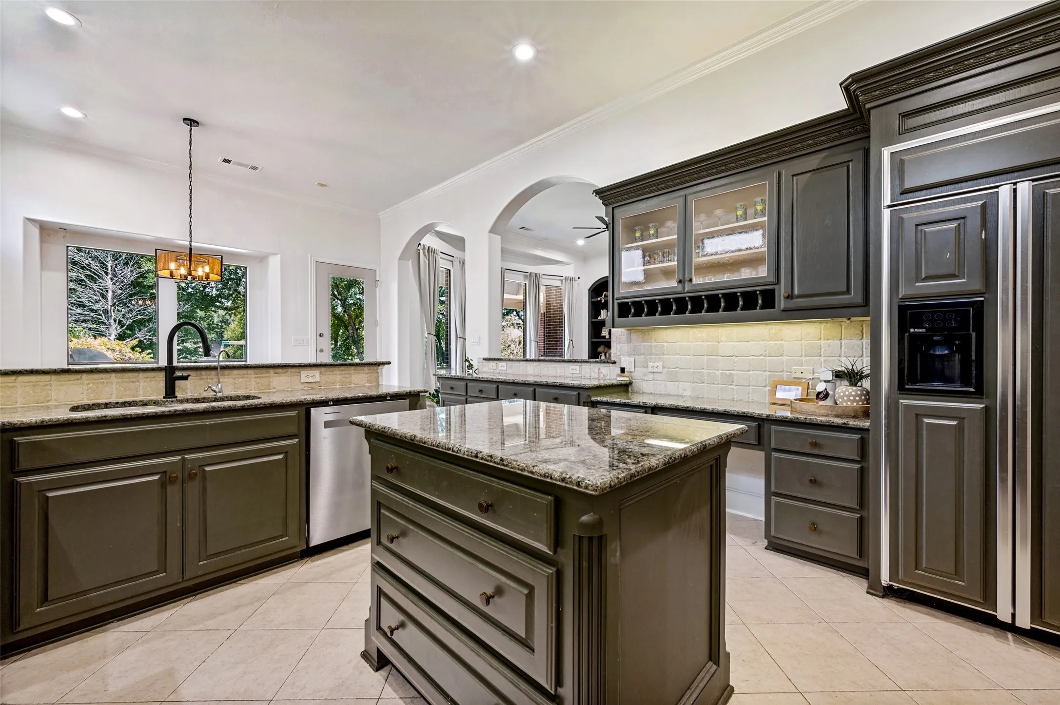 Kitchen featuring a central island, dark cabinetry, light-toned tile flooring, and integrated appliances