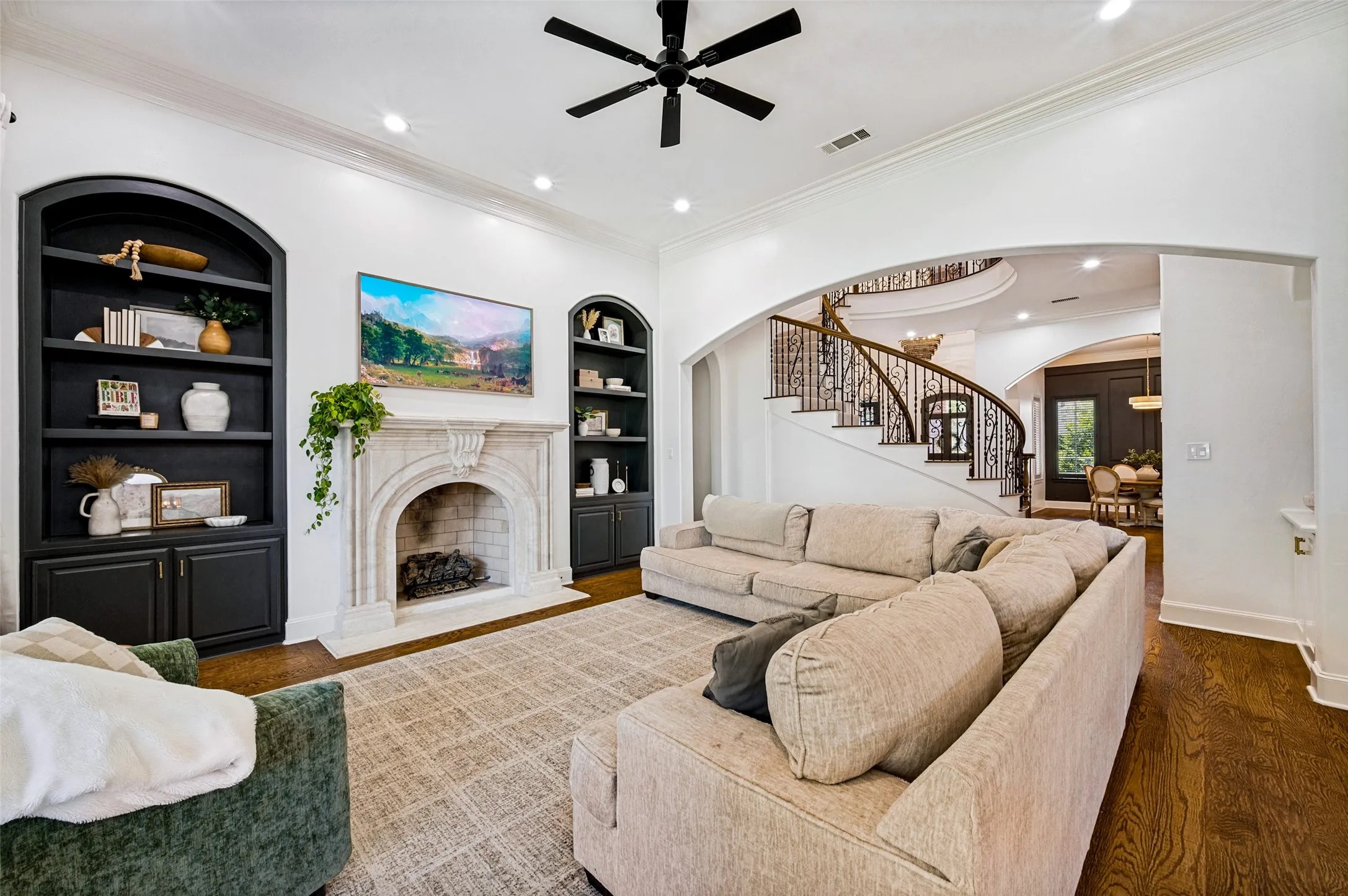 Living area featuring a detailed fireplace, arched built-in shelving, dark wood-finish flooring, recessed lighting, and a prominent spiral staircase with ornate railing