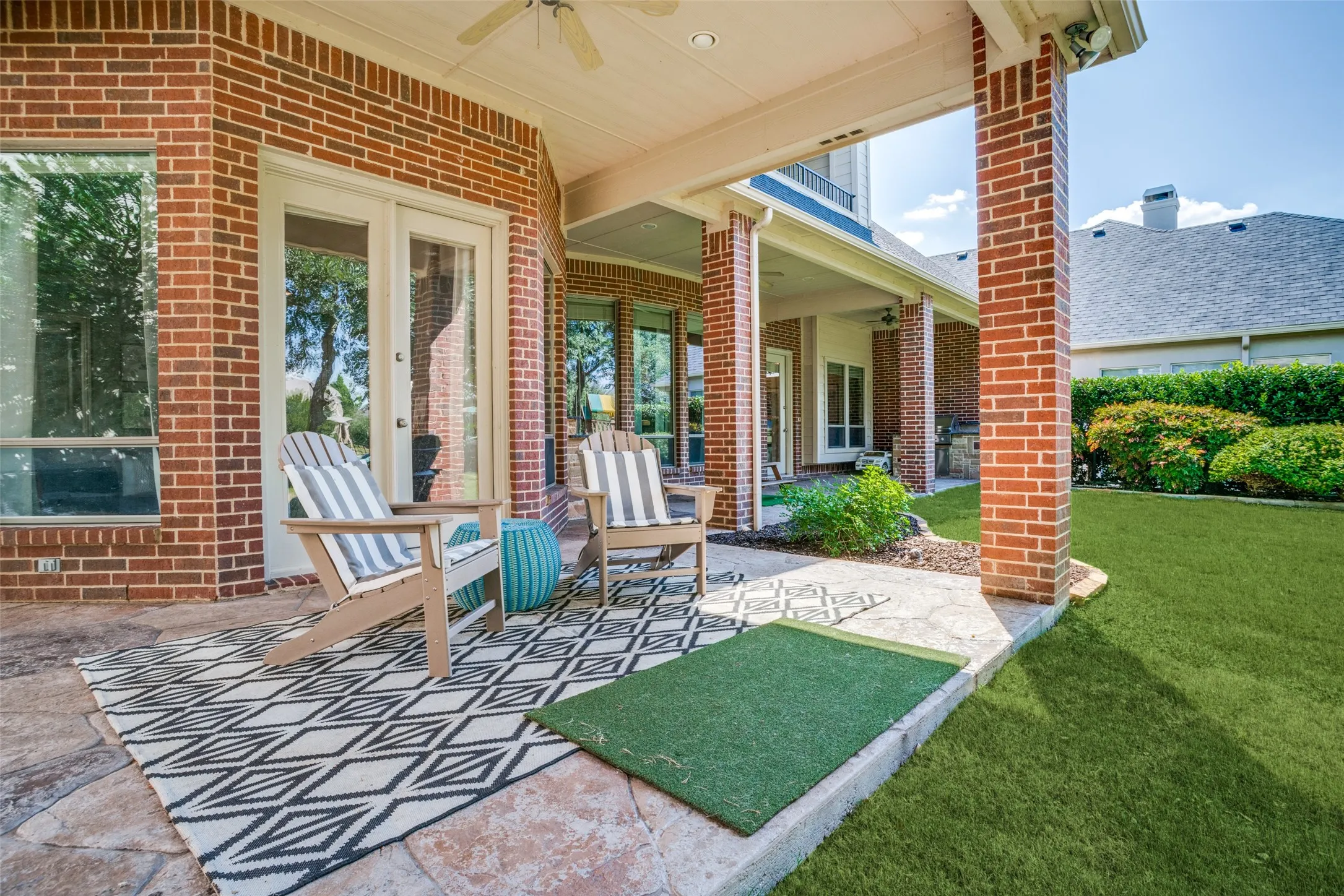 Expansive covered patio with brick columns and a ceiling fan, featuring a stamped concrete surface and manicured lawn