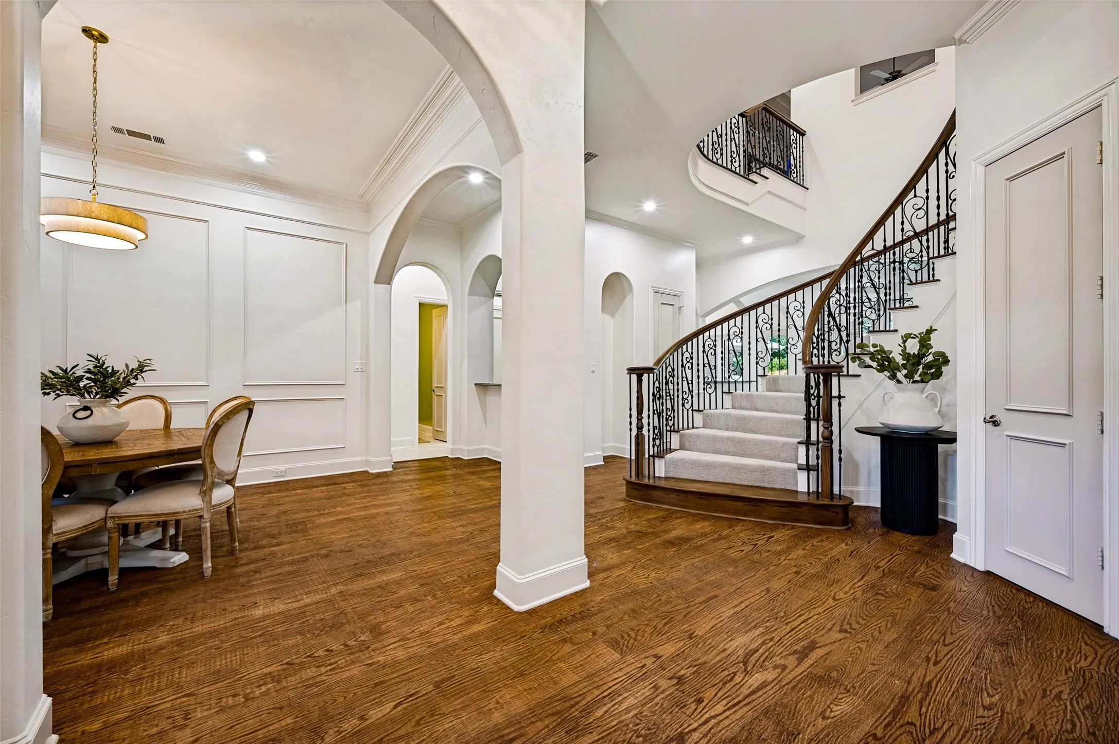 Rich wood-finish flooring throughout, featuring a grand curved staircase with ornate wrought iron balusters and wood handrails