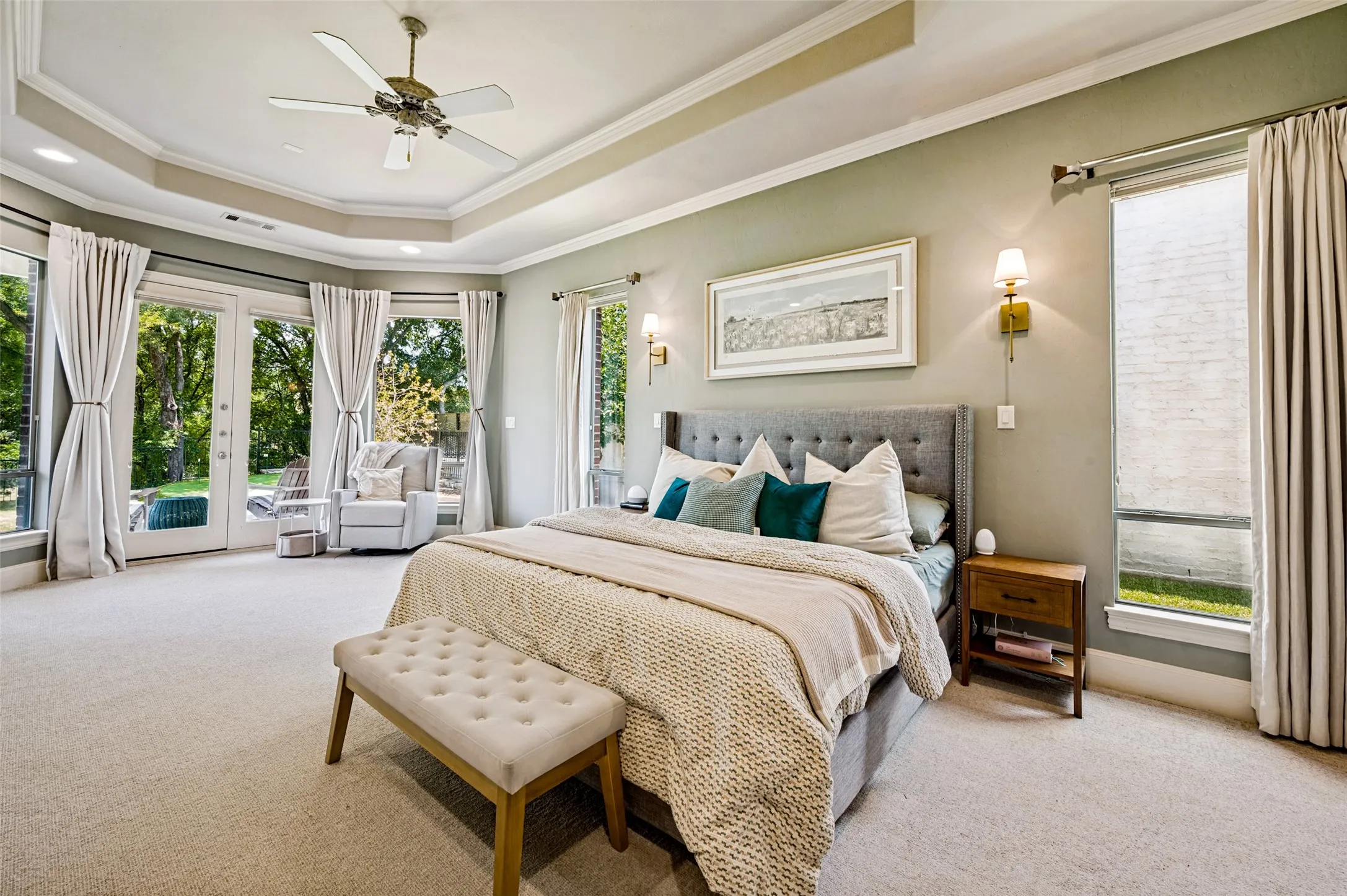 Tray ceiling with crown molding, ceiling fan, expansive windows, French doors, and wall sconces