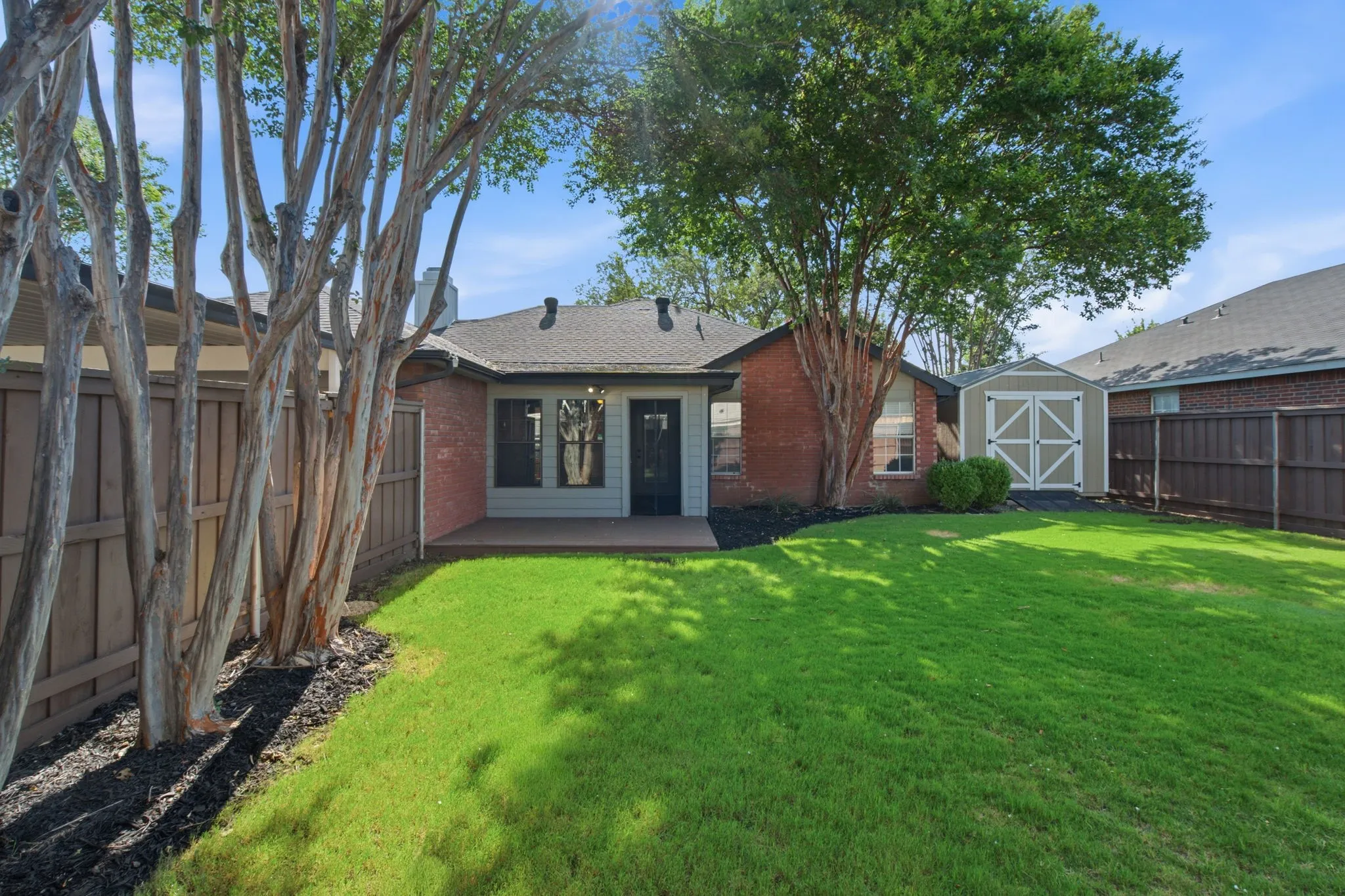 Spacious backyard featuring a manicured lawn, a wood-finish patio, and mature trees