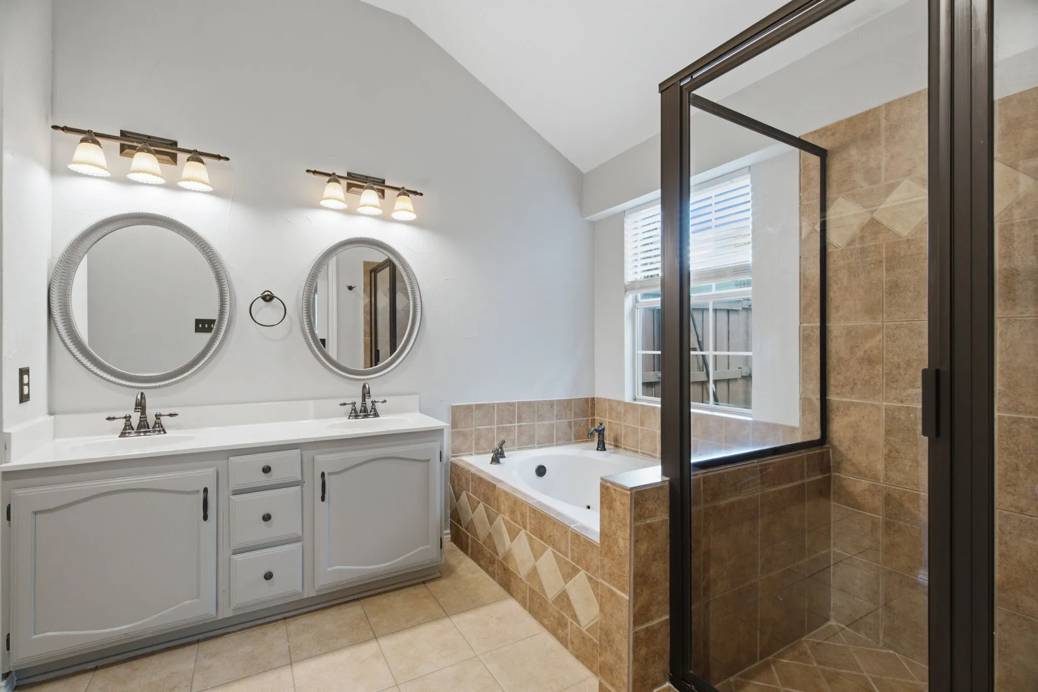 Dual vanity with gray cabinetry, round framed mirrors, and chrome fixtures
