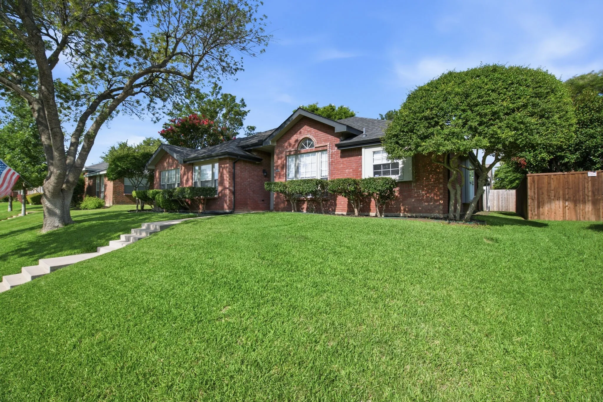Brick exterior home featuring a dark shingle roof, established landscaping, and a manicured lawn