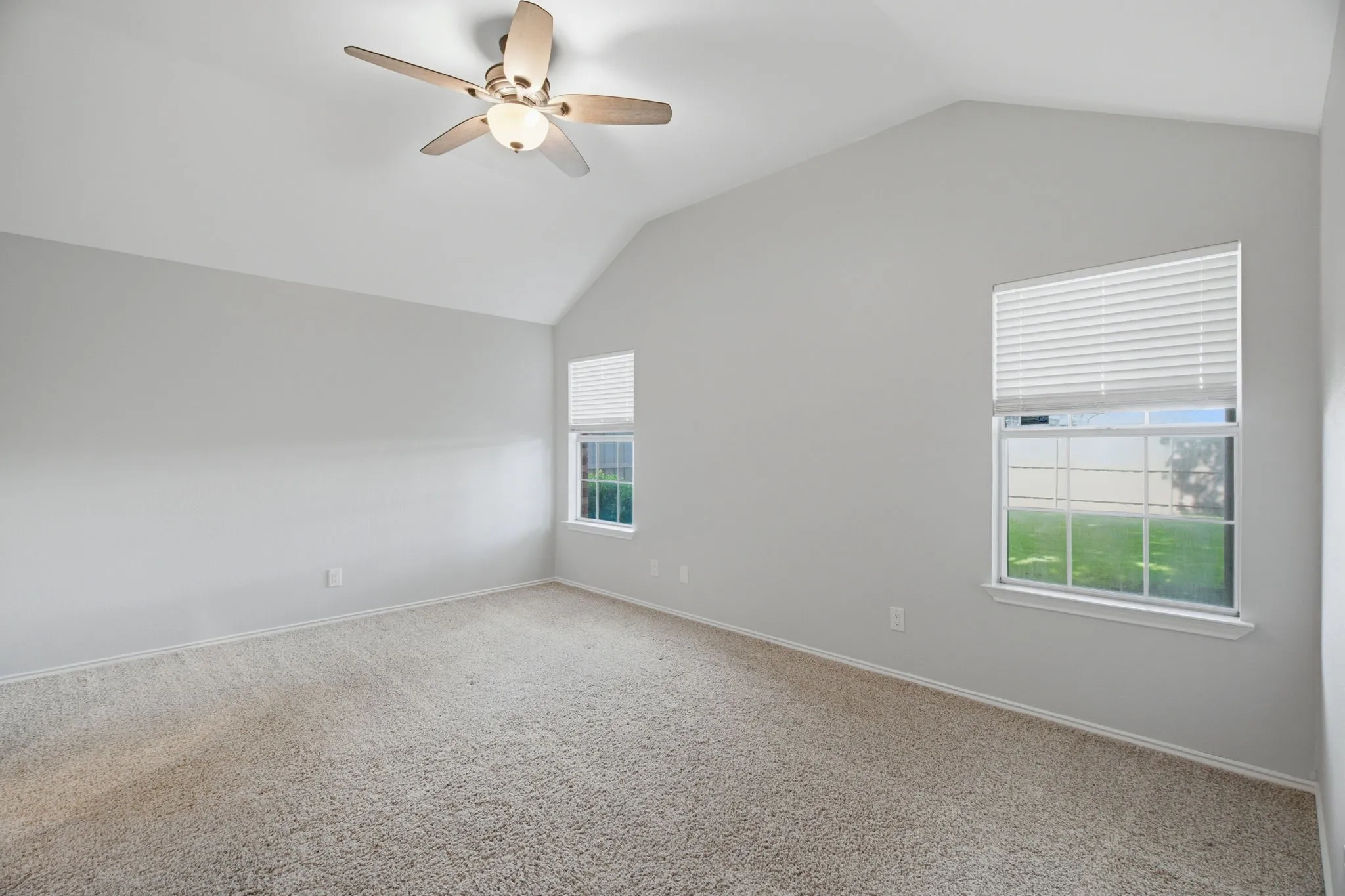 Vaulted ceiling with a ceiling fan light fixture, gray wall paint, and gray carpet flooring, virtually staged