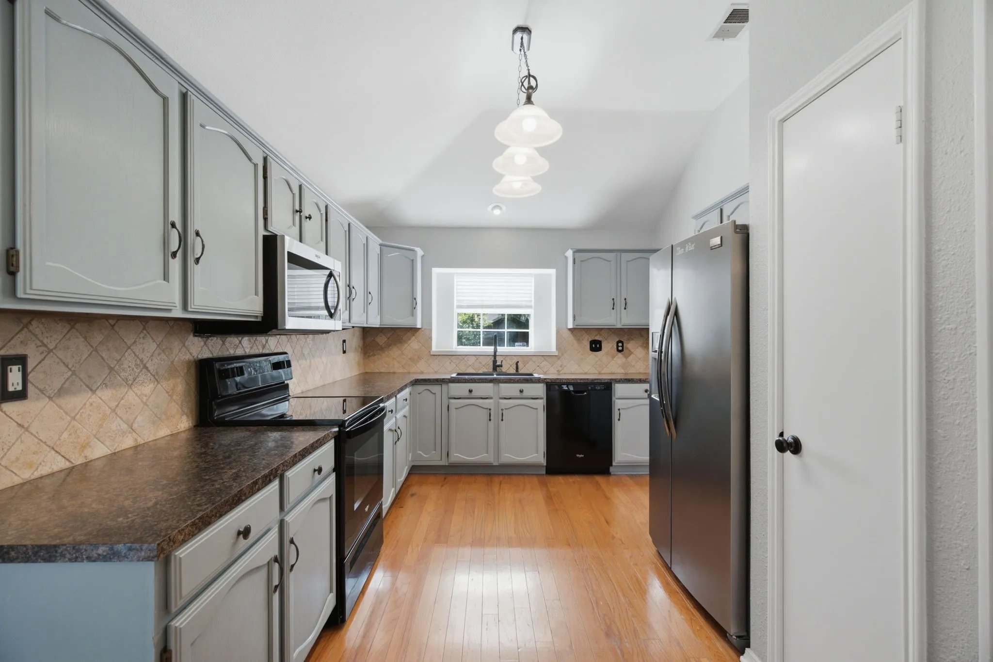 Kitchen featuring light gray cabinetry with dark hardware, brown laminate countertops, and a tiled backsplash