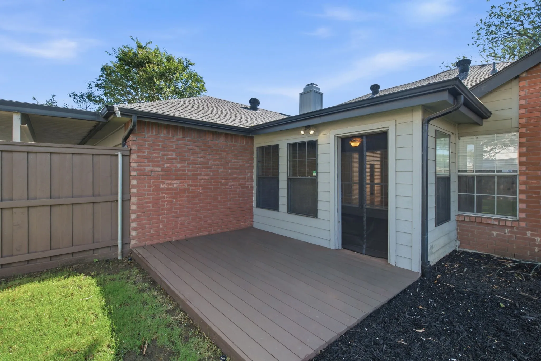 Composite decking patio with a screened door entry, surrounded by brick and horizontal siding