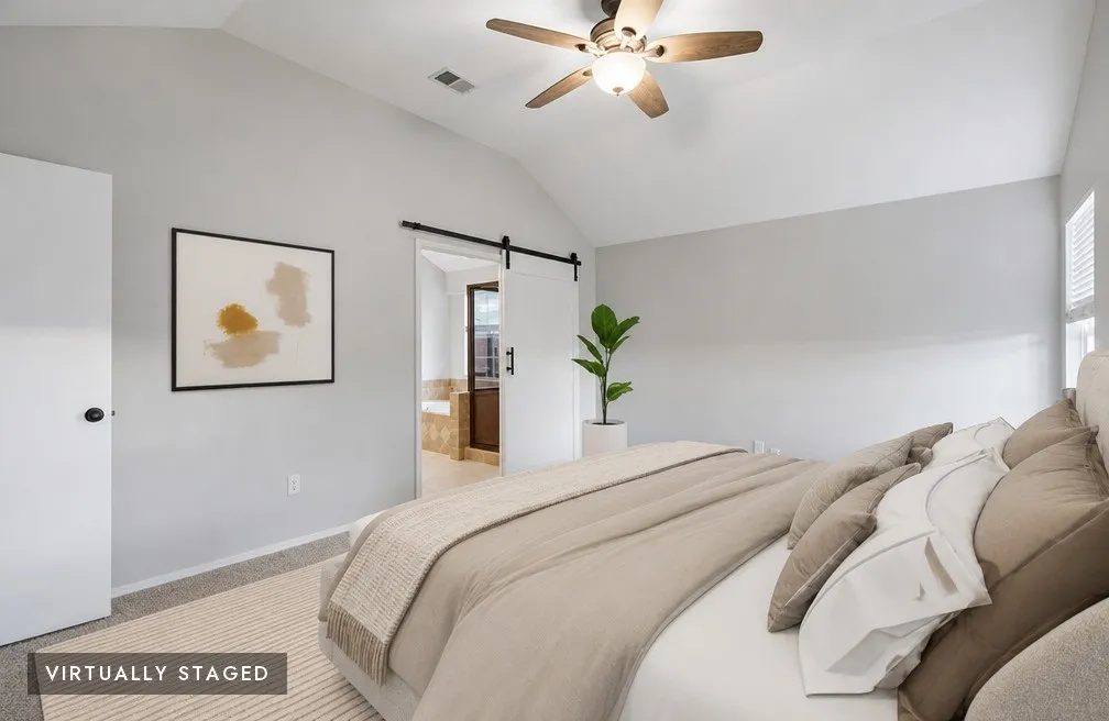 Vaulted ceiling featuring a ceiling fan, light gray wall finishes, carpet flooring, and a barn door entry, virtually staged