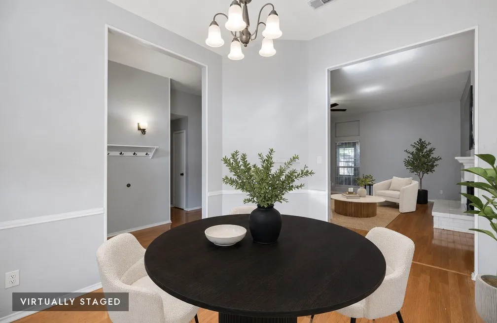 Dining area featuring a five-light chandelier, light gray walls with white wainscoting, and wood-finish flooring, virtually staged