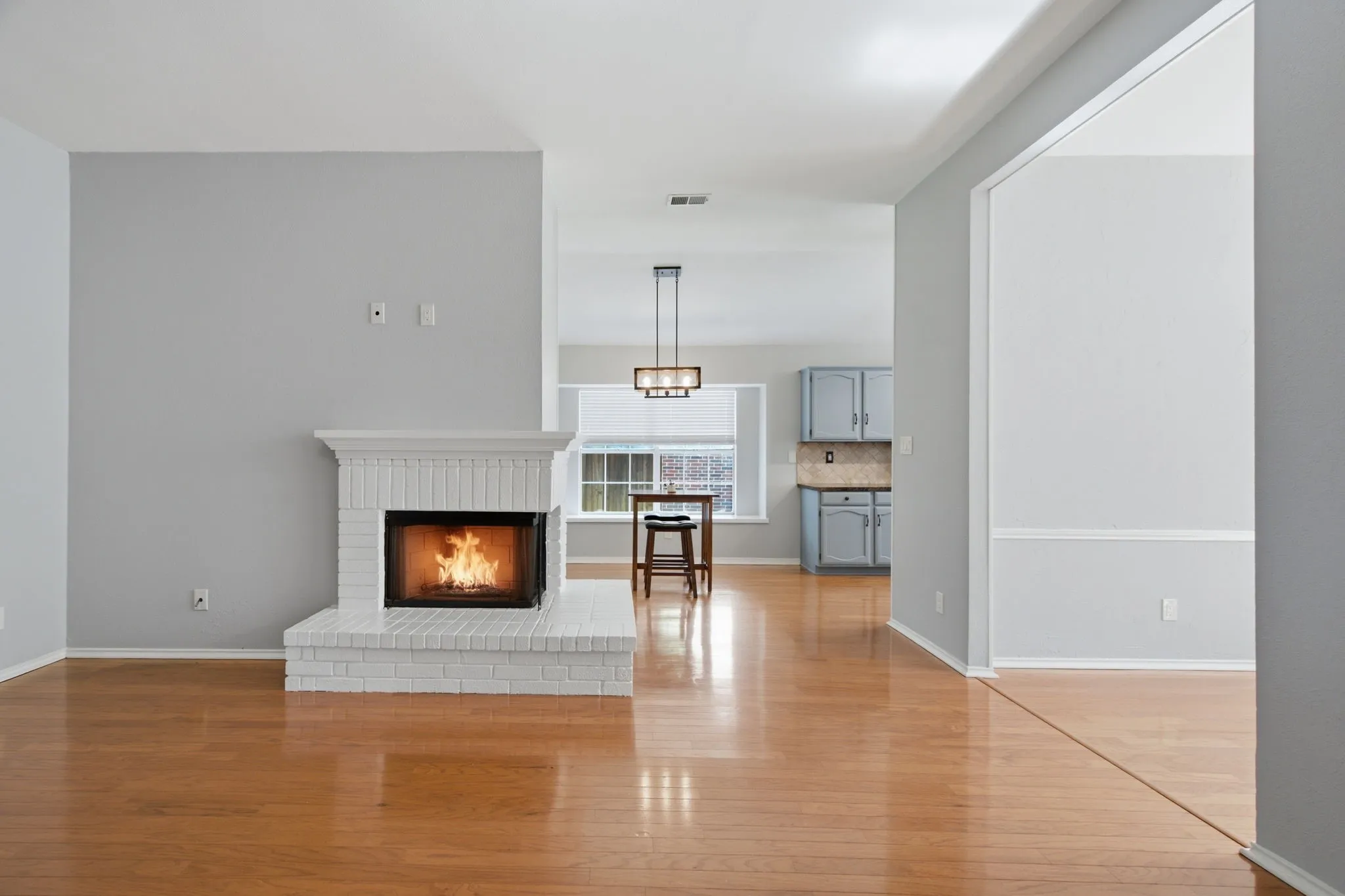 Living area with a white brick fireplace, wood-finish flooring, and recessed lighting