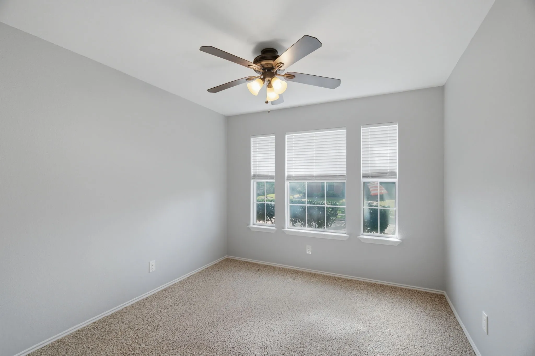 Carpeted room featuring three windows with blinds, a ceiling fan with integrated lighting, and light-colored walls