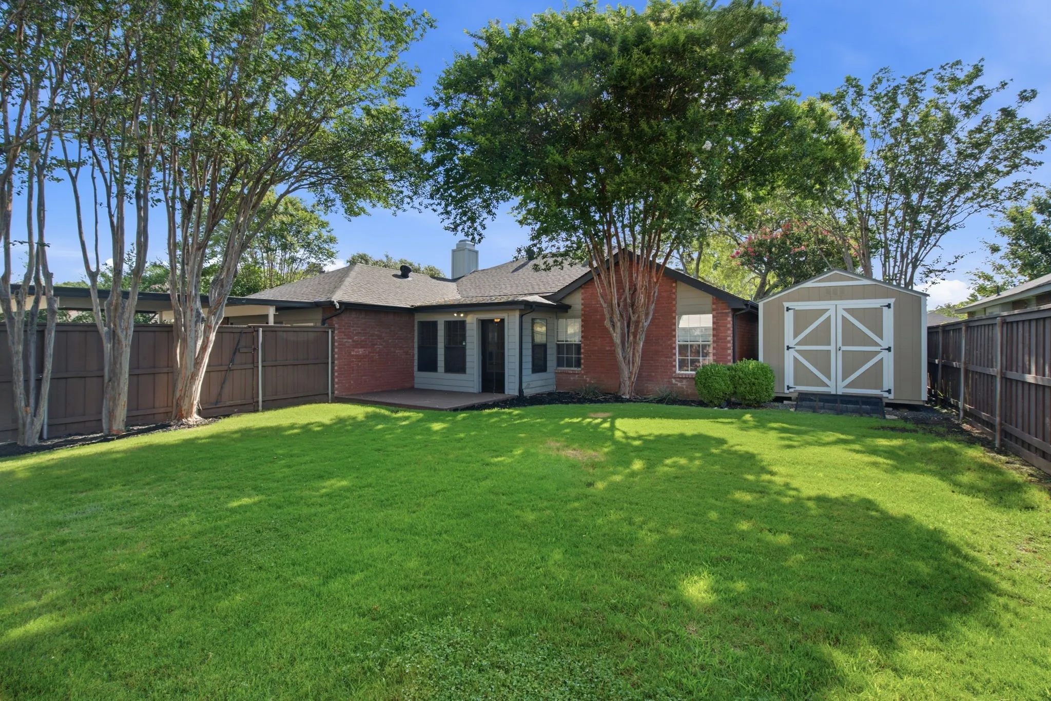 Expansive backyard featuring a manicured lawn, full privacy fencing, mature trees, and a detached storage shed
