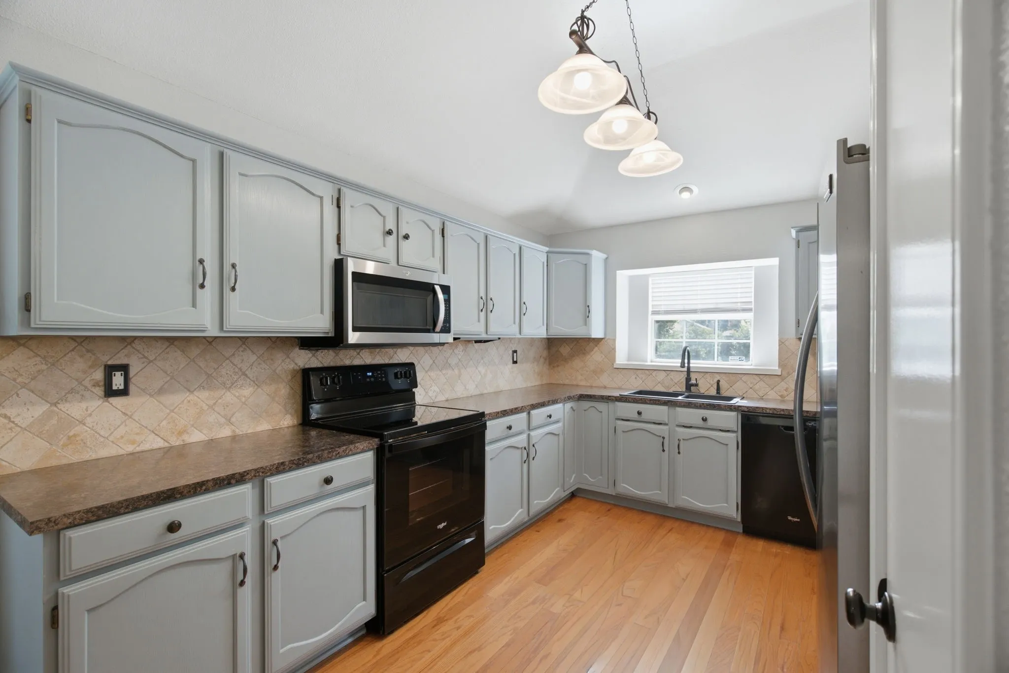 Kitchen featuring light blue cabinetry, mosaic tile backsplash, wood-finish flooring, and a window above the sink