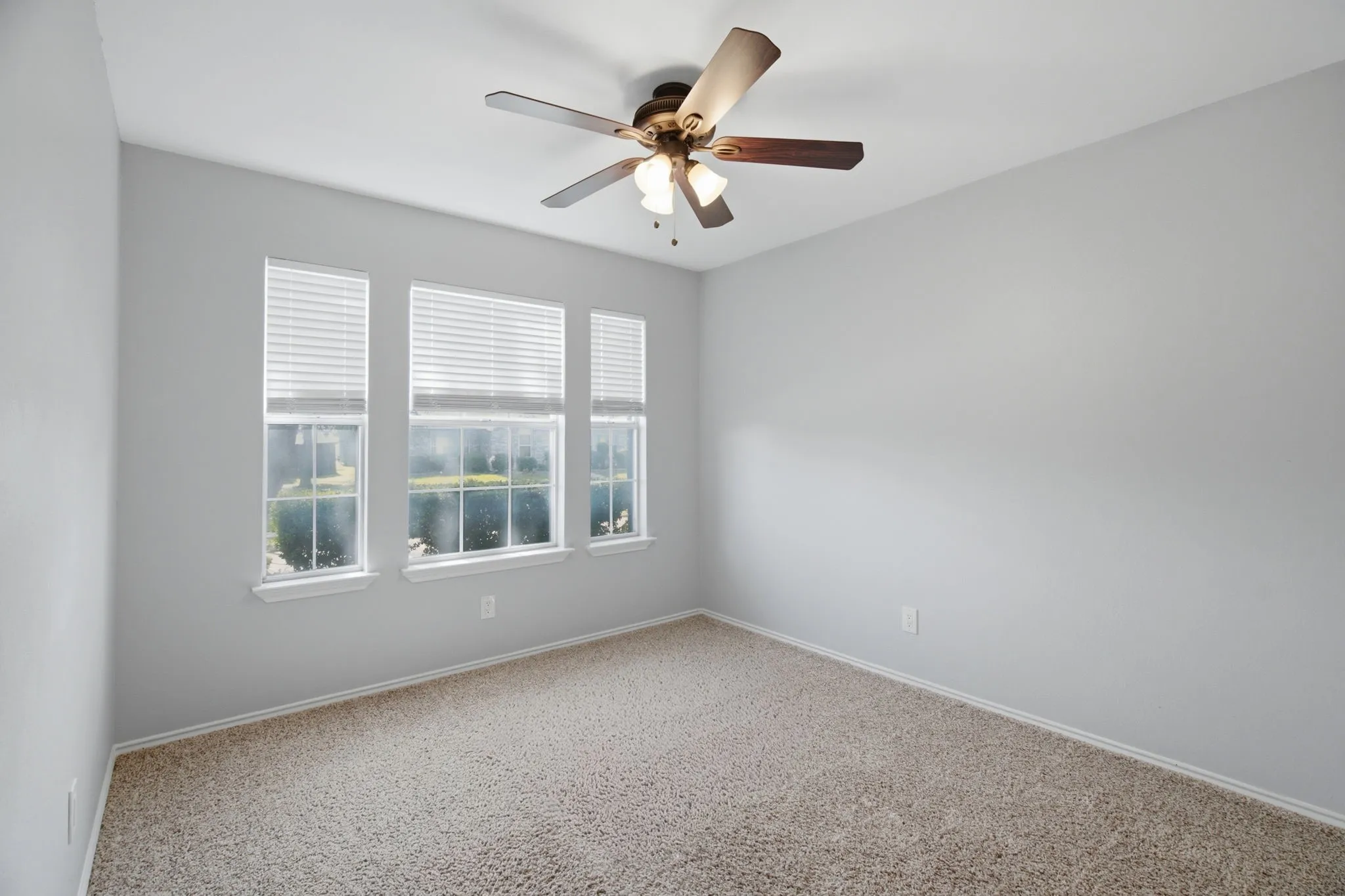 Bright room featuring three windows with horizontal blinds, neutral wall paint, textured carpet flooring, and a ceiling fan with integrated lighting