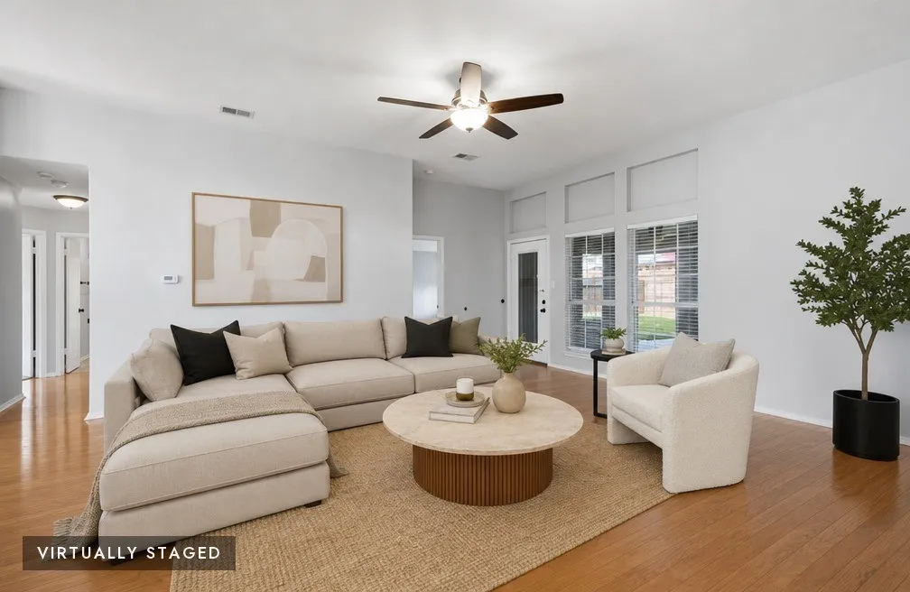 Spacious living area featuring light wood-finish flooring, a ceiling fan, and abundant natural light from multiple windows, virtually staged