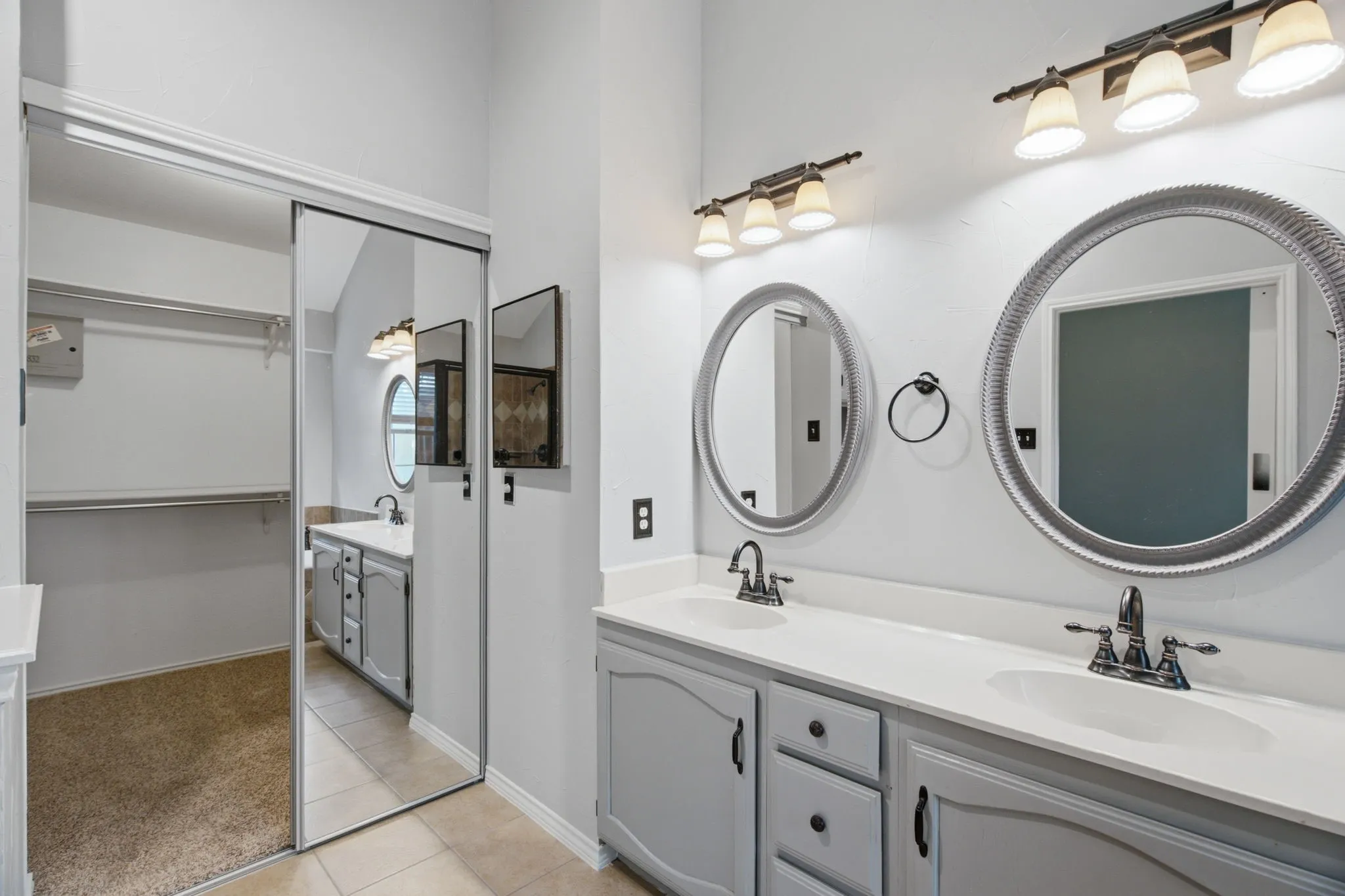 Dual vanity with white countertops and undermount sinks, featuring chrome faucets and overhead four-bulb light fixtures