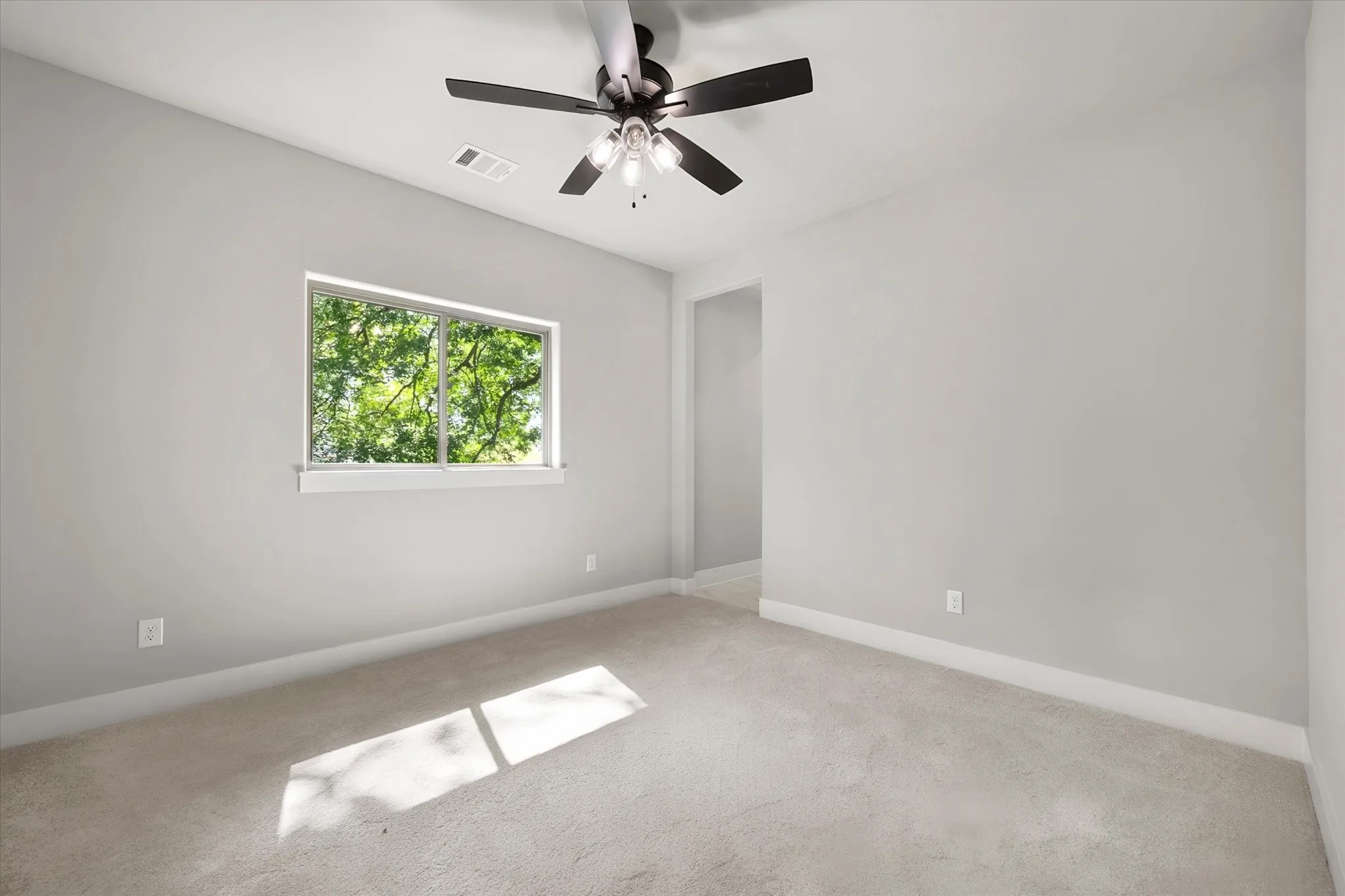 Carpeted flooring, light gray wall paint, white trim, ceiling fan with integrated lighting, and a single window
