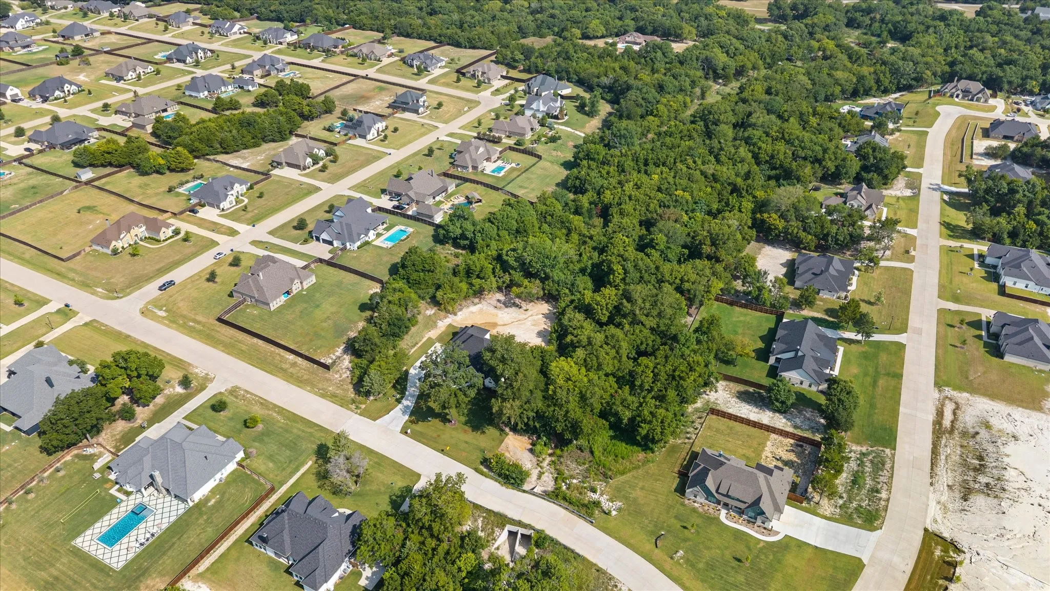 Aerial perspective highlighting a developed residential neighborhood with structured streets, individual properties with green landscaping, and dense natural tree coverage