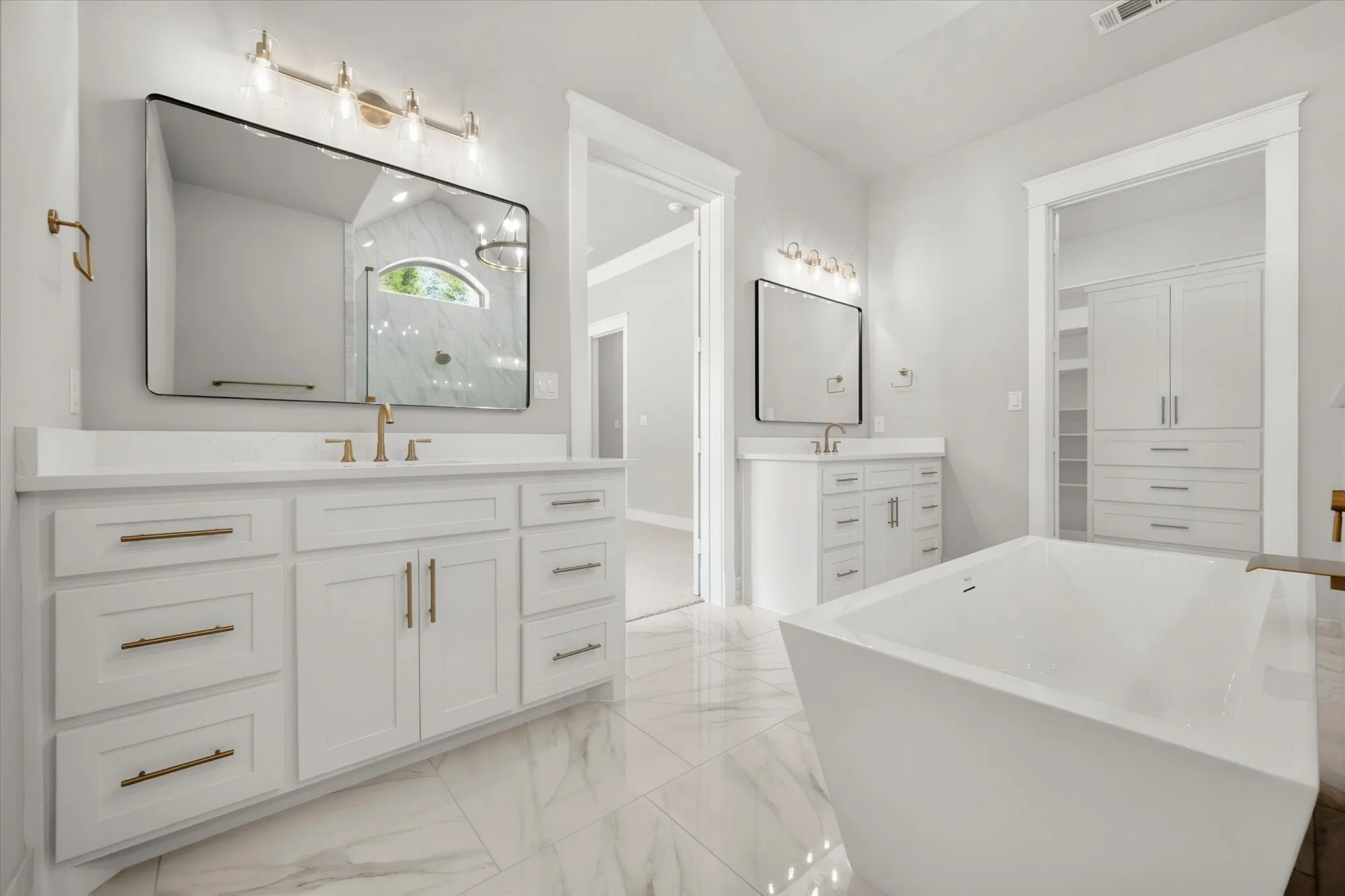 Dual white vanities with gold-tone hardware, a freestanding soaking tub, and tile flooring