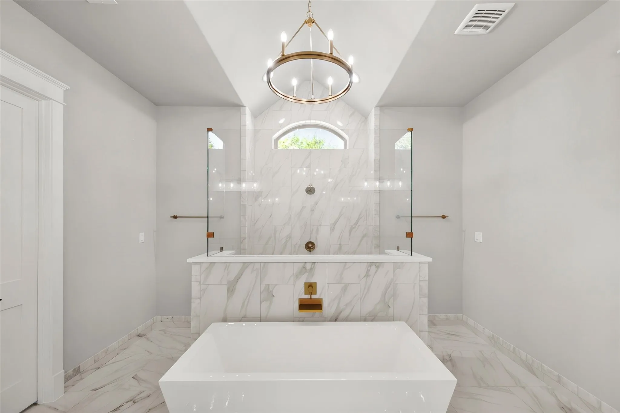 Freestanding soaking tub, large format marble-look tile flooring, marble-look tile shower surround, arched window, and a chandelier lighting fixture
