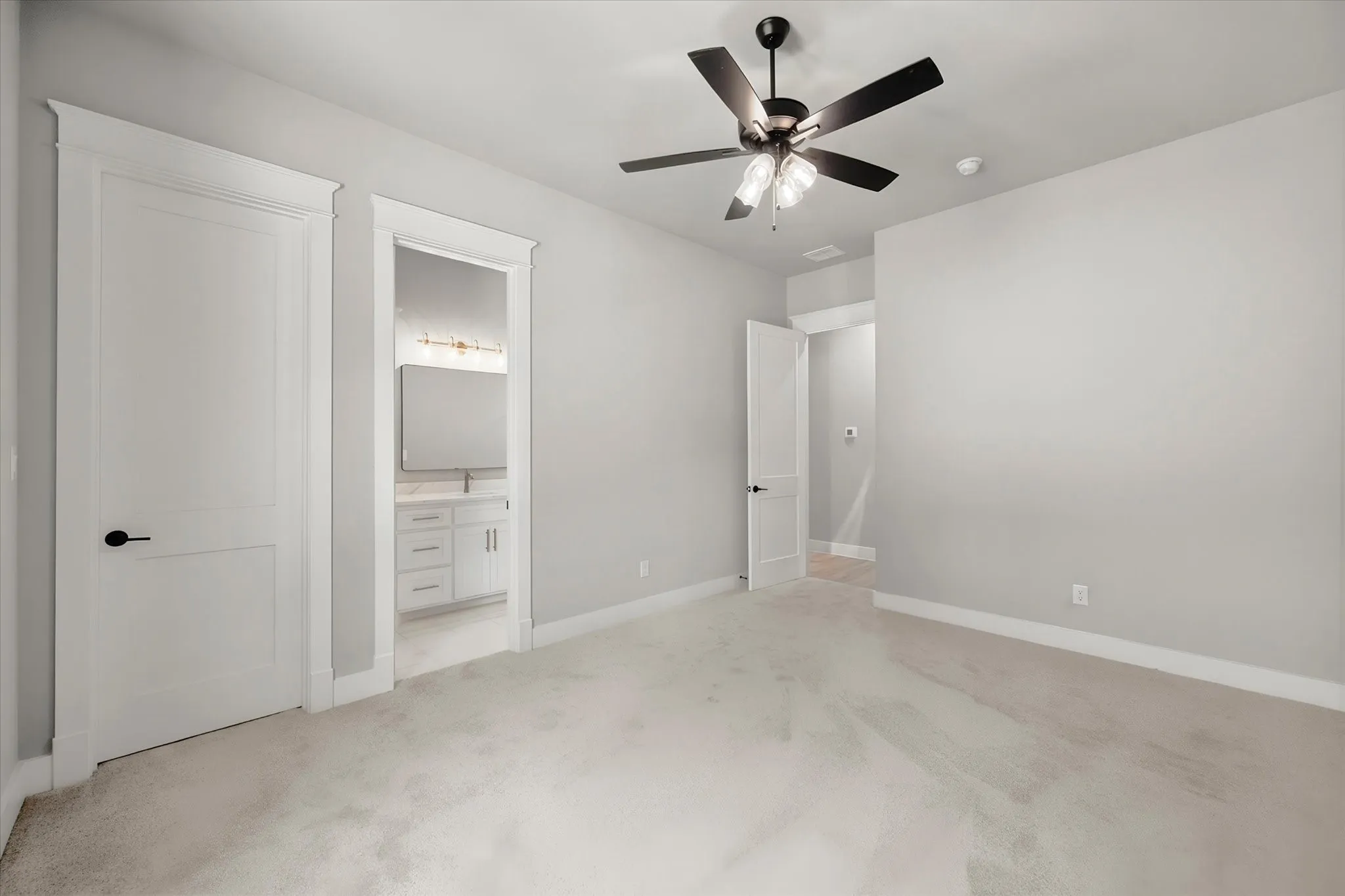 Plush carpeted flooring with light gray walls, a ceiling fan with integrated lighting, and a white vanity with a rectangular mirror