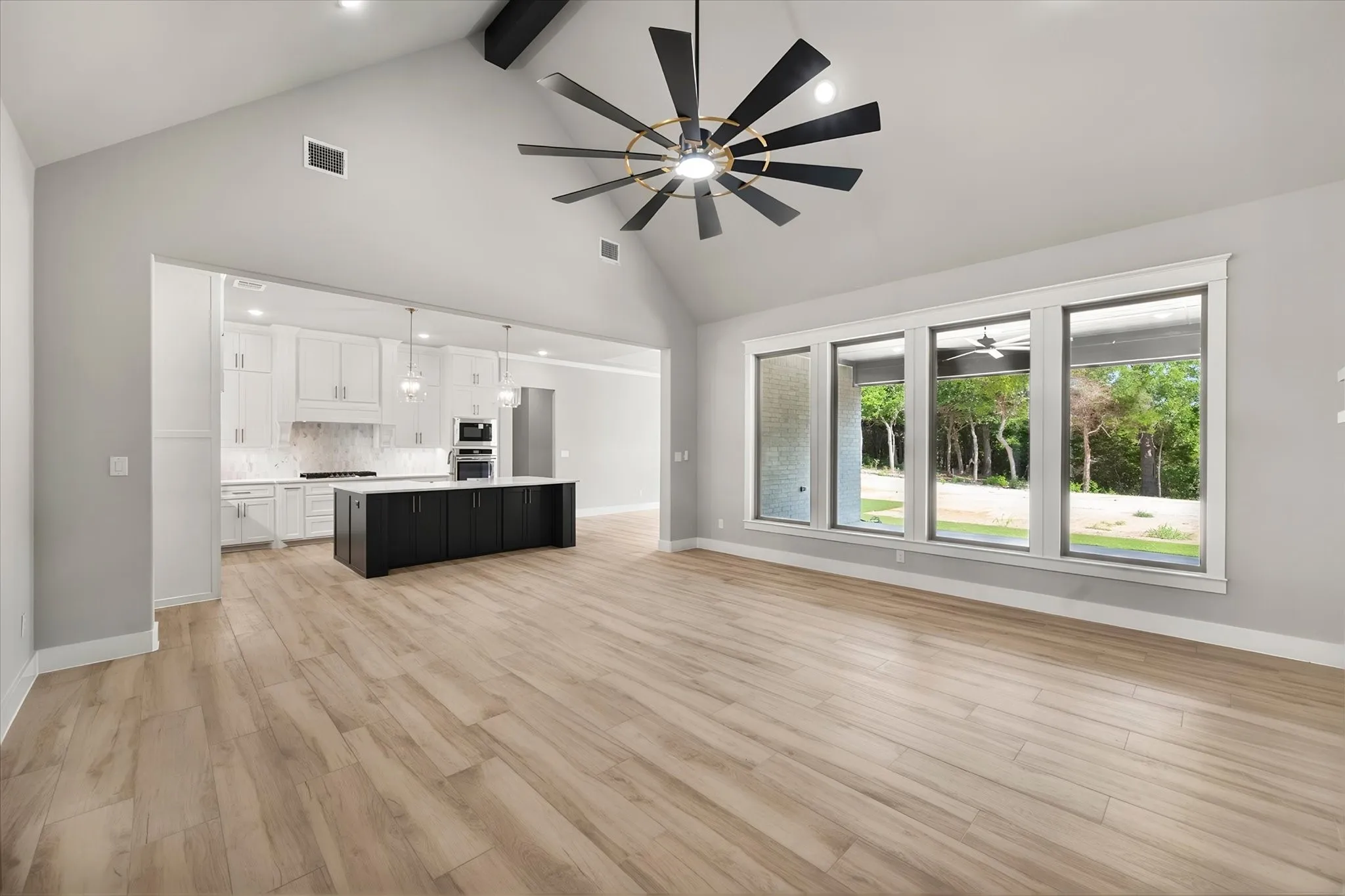 Open-concept living space featuring engineered wood-finish flooring, soaring vaulted ceilings with modern black ceiling fan, and expansive multi-panel sliding glass doors overlooking mature landscaping