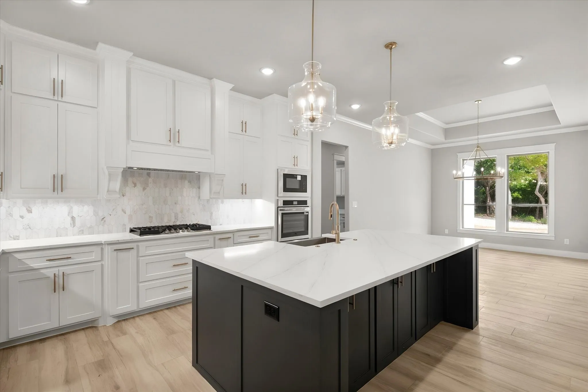 White cabinetry with brass hardware, a large kitchen island with a white countertop, stainless steel double ovens, and a gas range