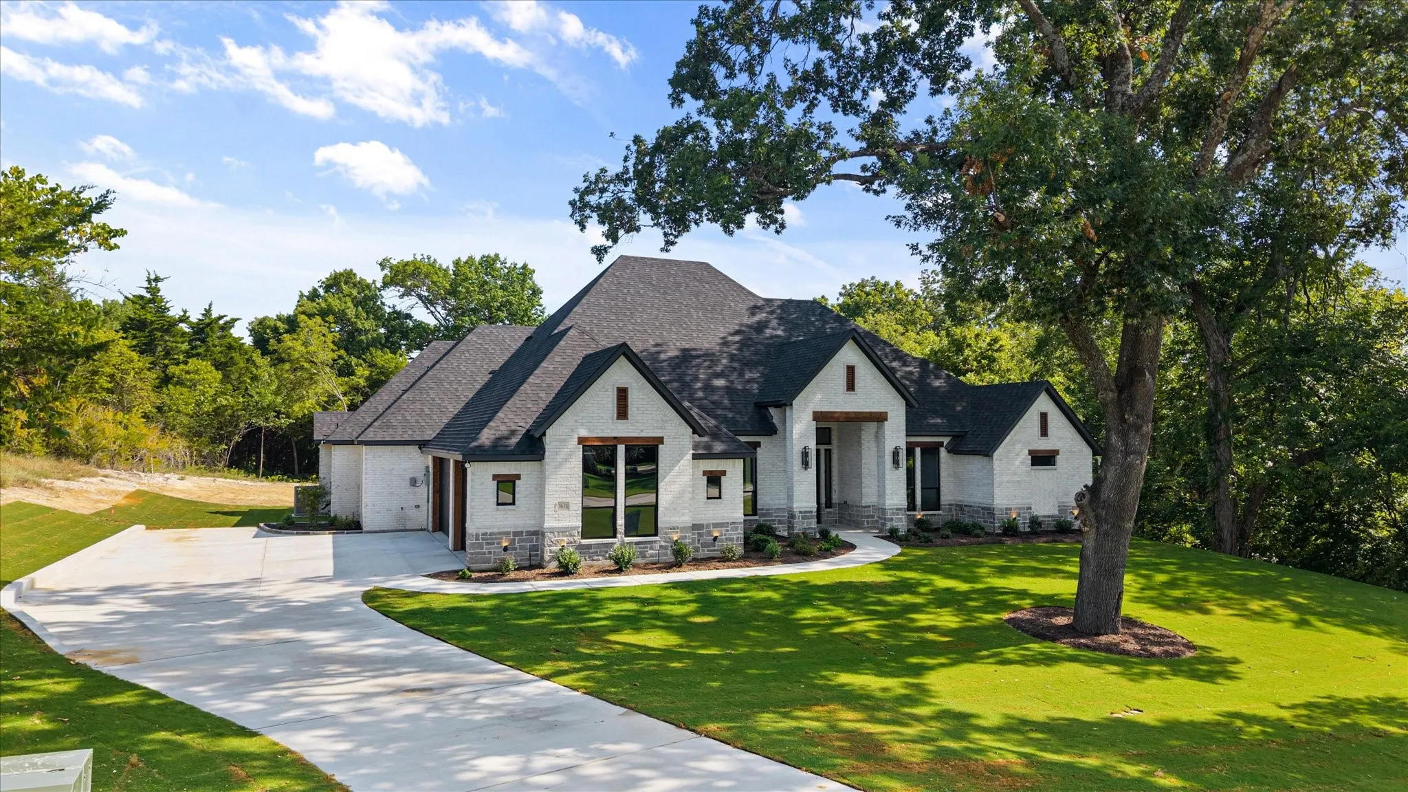 Contemporary exterior featuring light brick and stone accents, a dark shingle roof, a concrete driveway, and established front yard landscaping